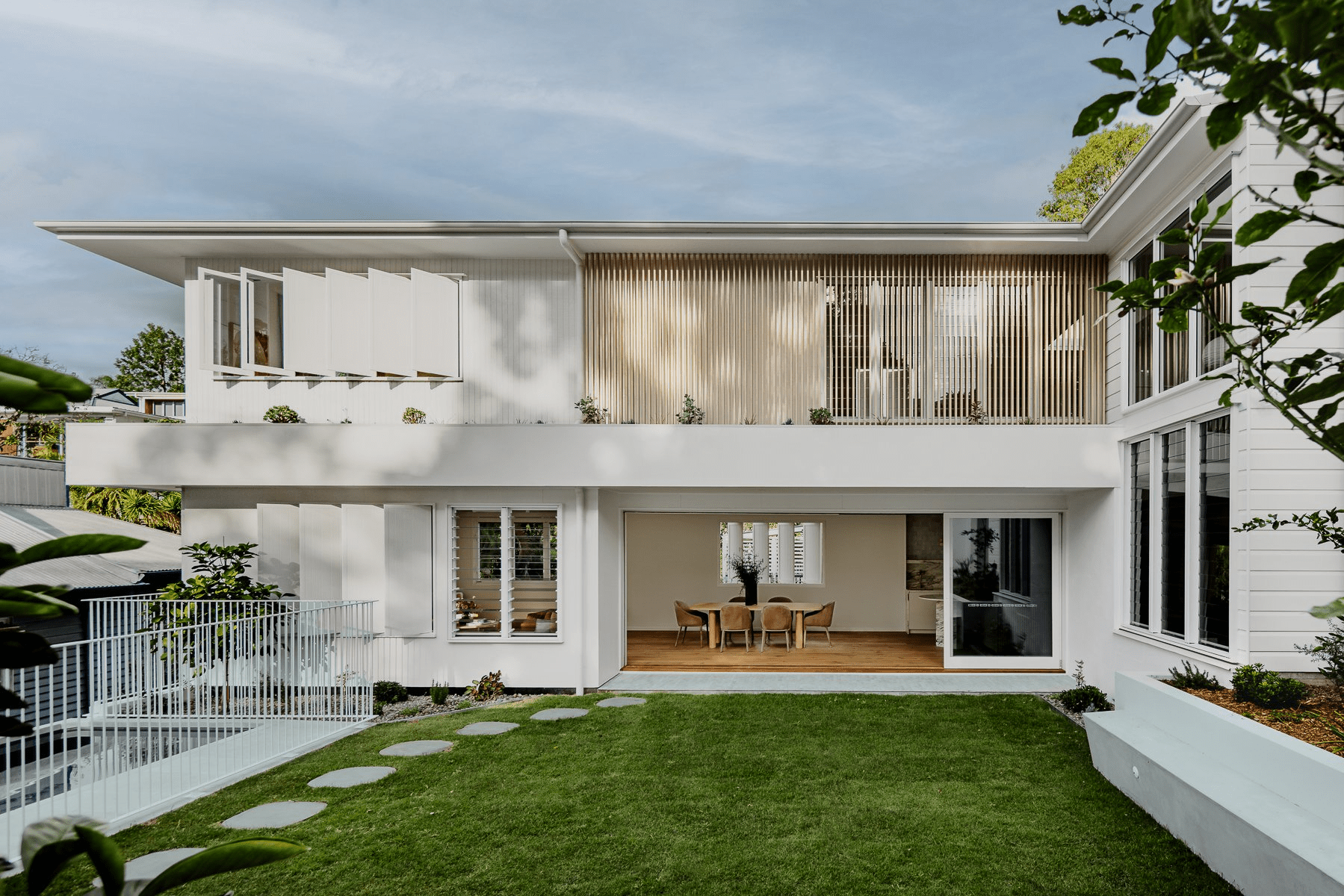 Hazlewood House by Favell Architects. Photography by Andy Macpherson. Backyard of double storey white clad renovated cottage. Green grass. Doors open from dining space to backyard. 