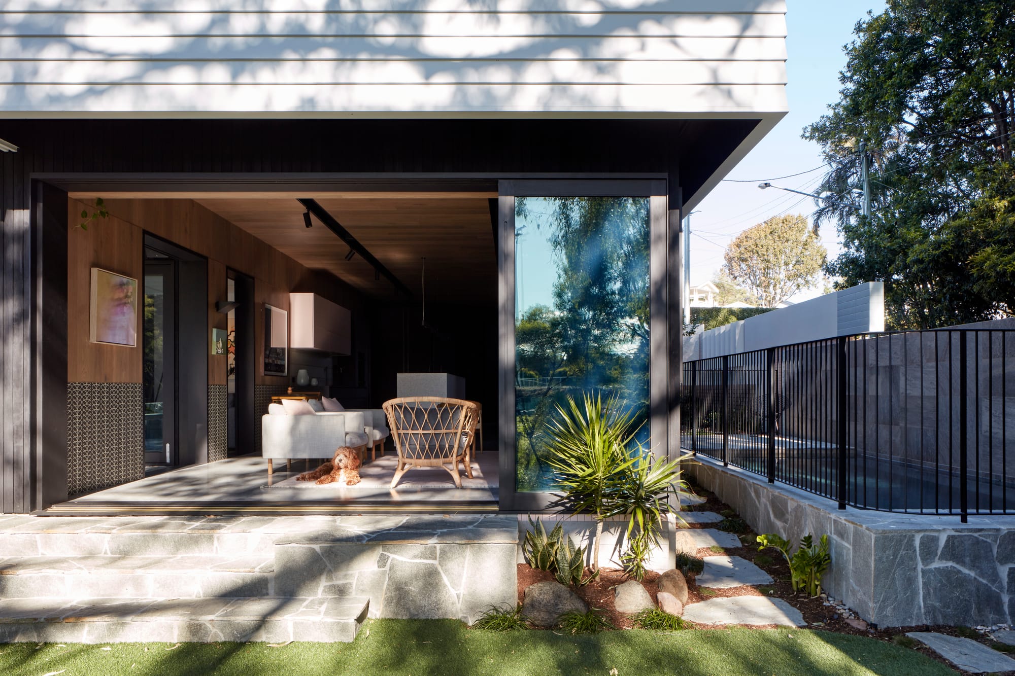Uxbridge House by Tim Stewart Architects. Photography by Christopher Frederick Jones. Exterior of home with stone steps leading to indoor living area. Green grass and fenced pool to left. 