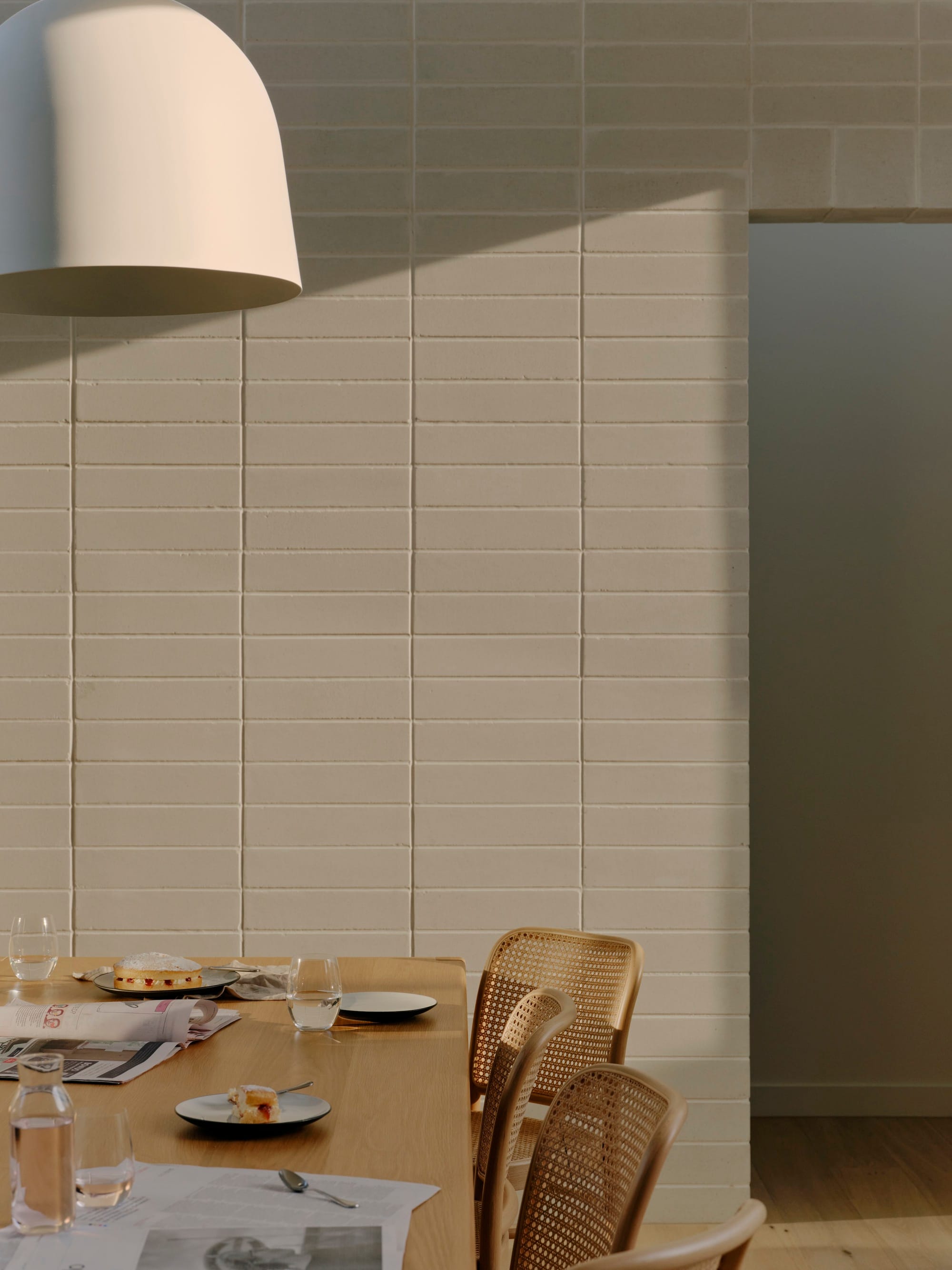 Wheatland House by Tom Roberston Architects. Photography by Tom Ross. White brick wall behind timber dining table with timber and rattan dining chairs. 