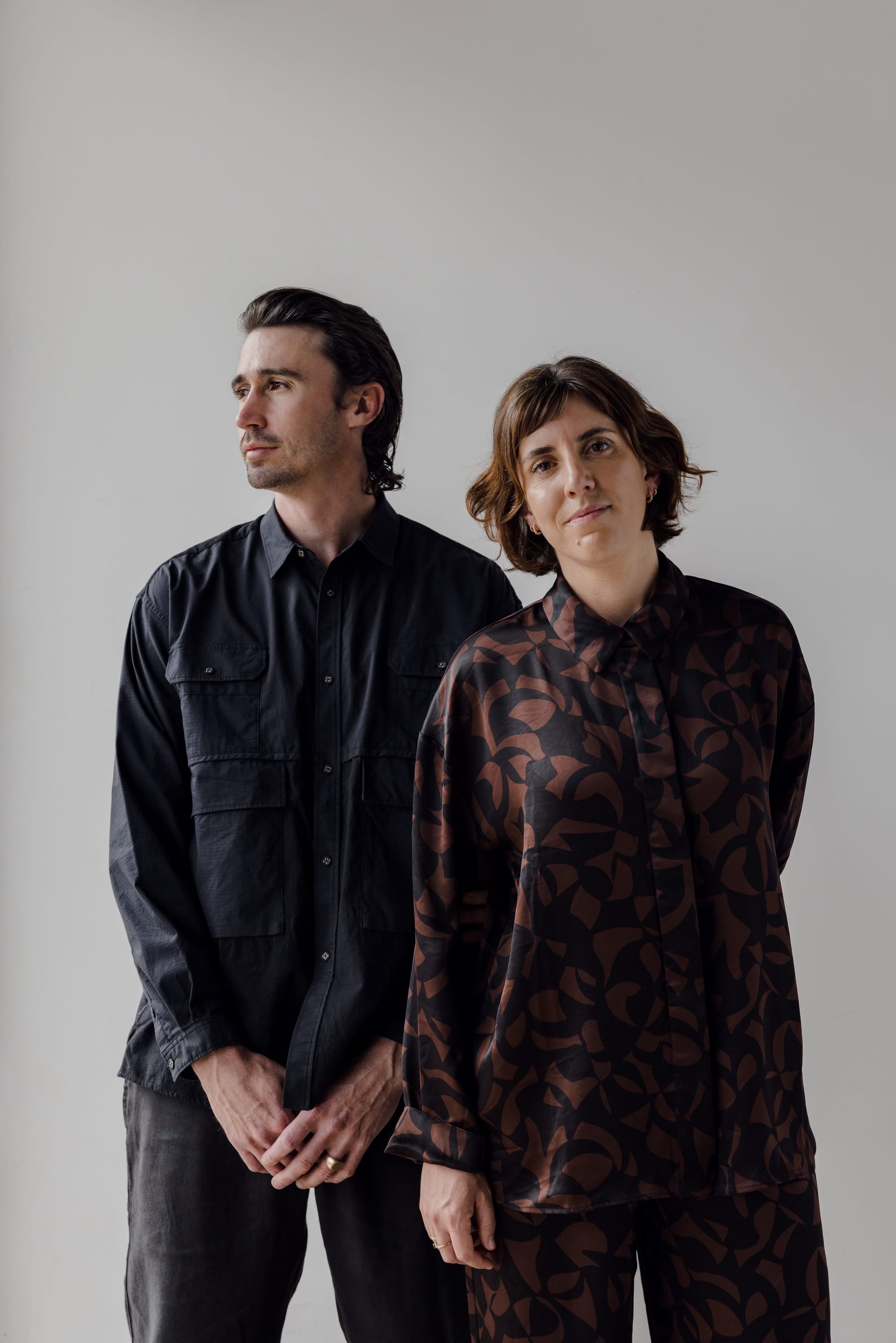 Amanda and Harrison of Otetto. Image copyright of Otetto. Woman in graphic print matching set stands next to man in all black outfit in front of industrial backdrop.
