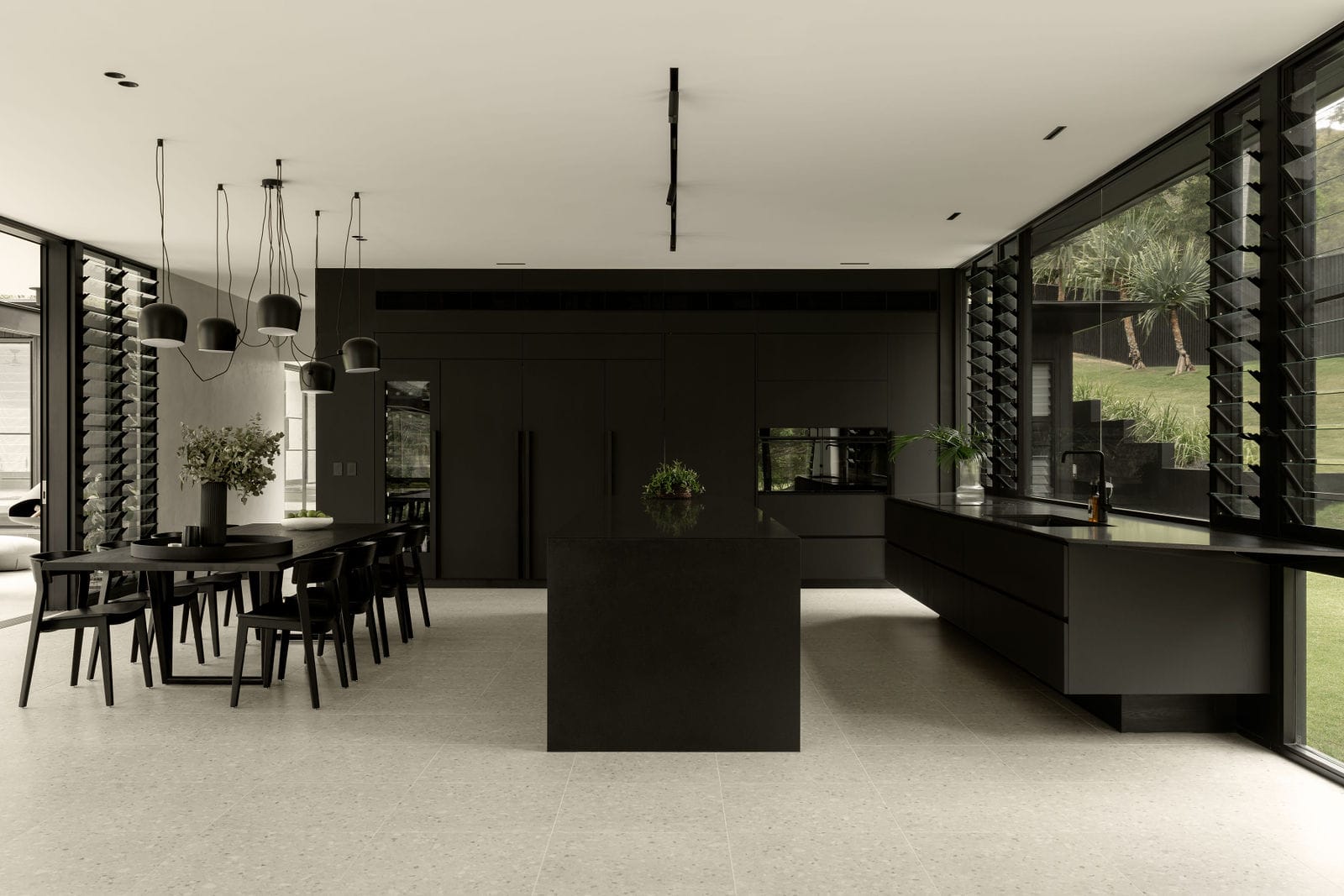 Blackwood by Sarah Waller Architecture. Photography by Alyne Media. Black kitchen with polished concrete floor tiles. Black dining set with black pendant lighting. 