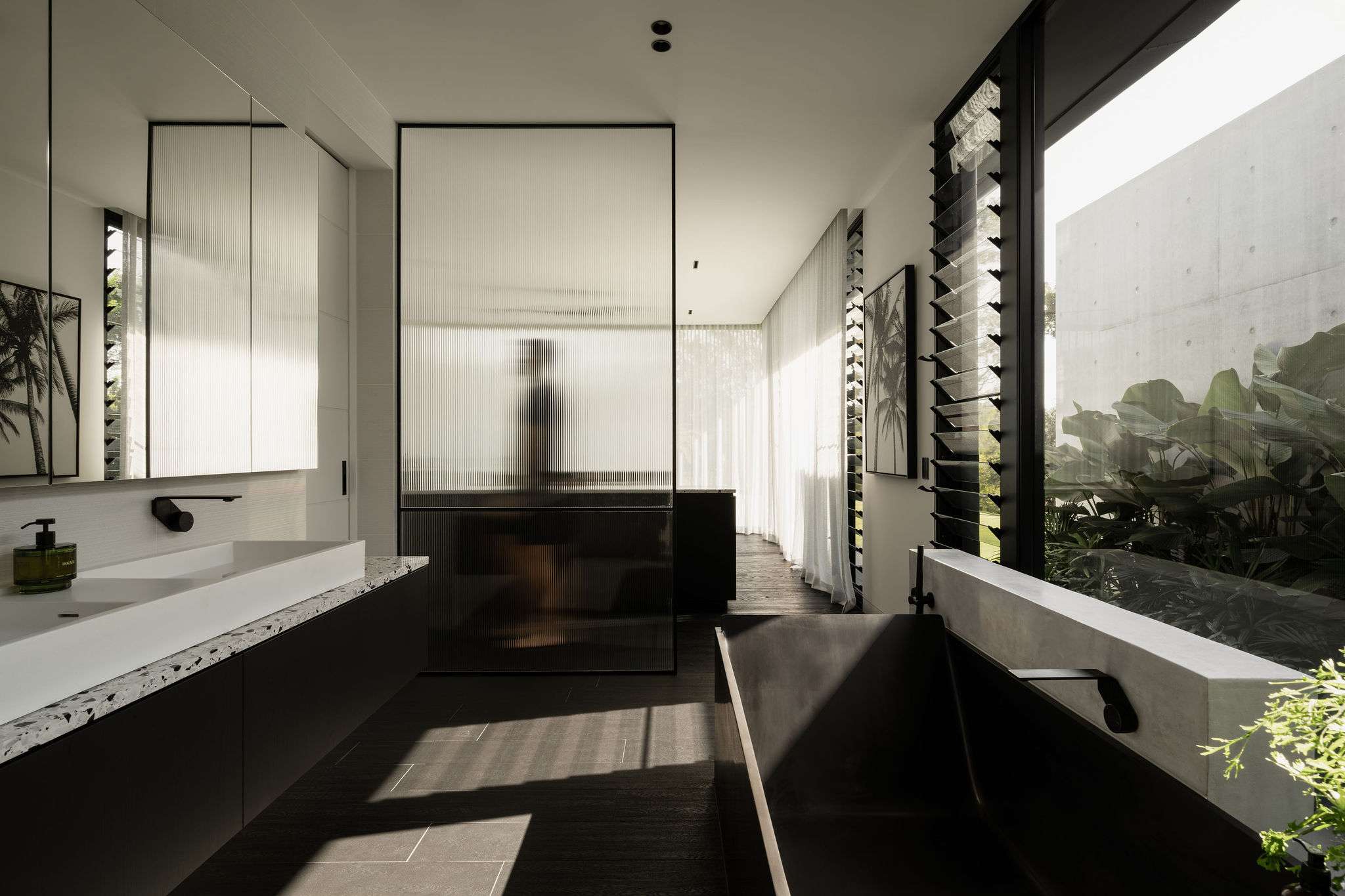 Blackwood by Sarah Waller Architecture. Photography by Alyne Media. Bathroom with fluted glass shower screen. Terrazzo countertops run length of room. Black floors. 