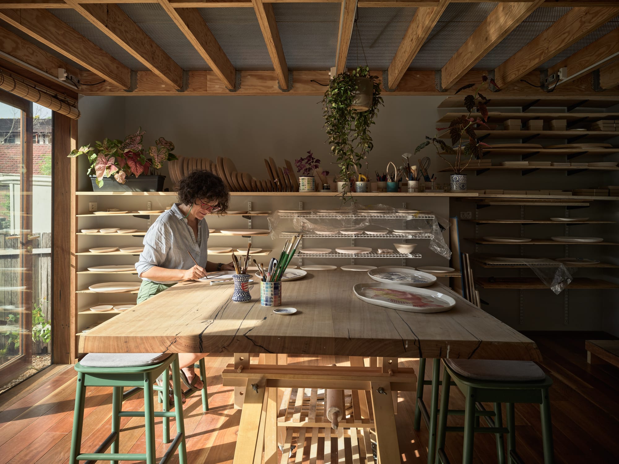 Coconut Crab by Alexander Symes Architect. Photography by Barton Taylor Photography. Interior studio with timber work desk, exposed timber beams and timber floors. Wall of shelves in background.