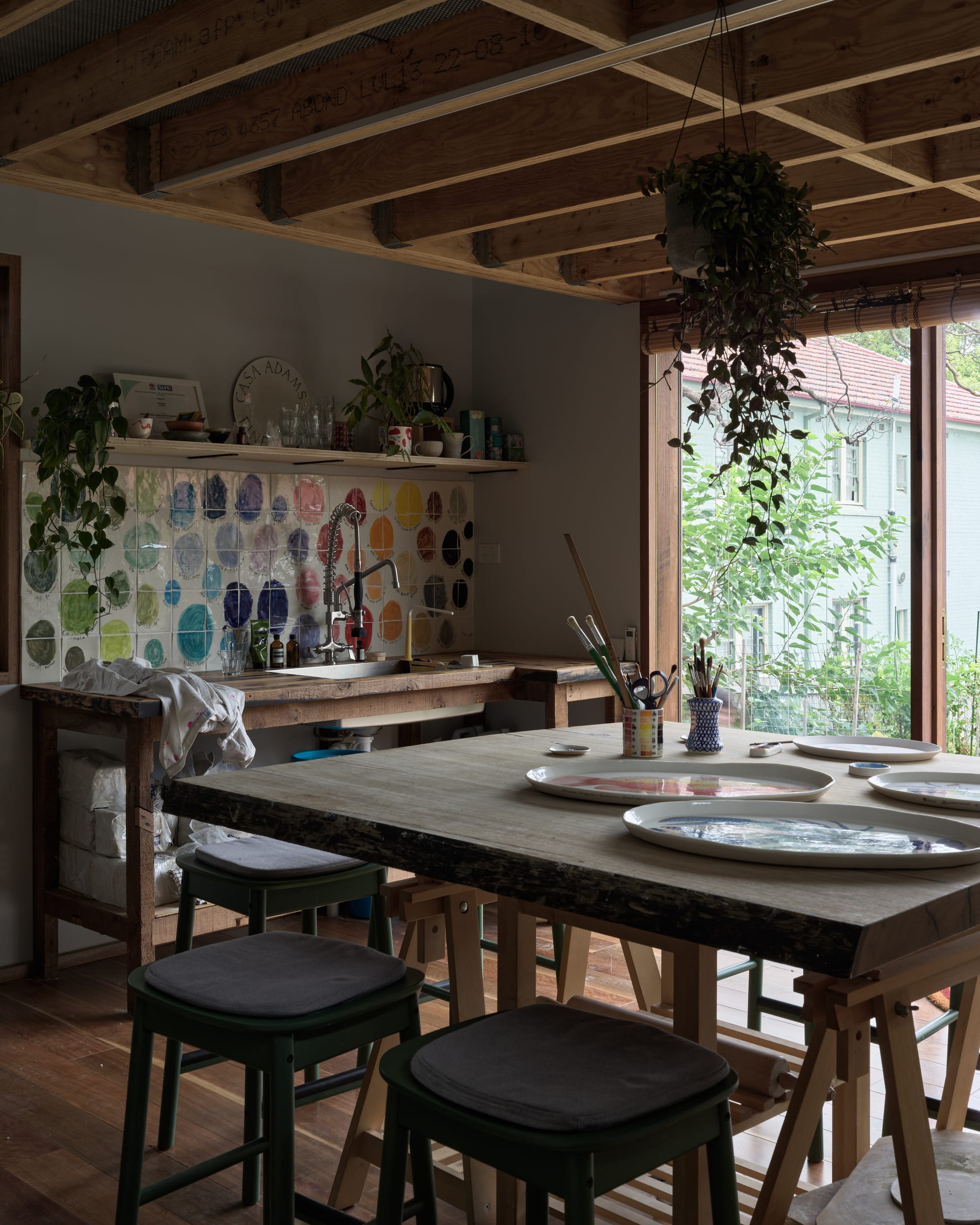 Coconut Crab by Alexander Symes Architect. Photography by Barton Taylor Photography. Art studio interior with square timber table and stools. Freestanding timber bench and sink with multi-coloured splashback.