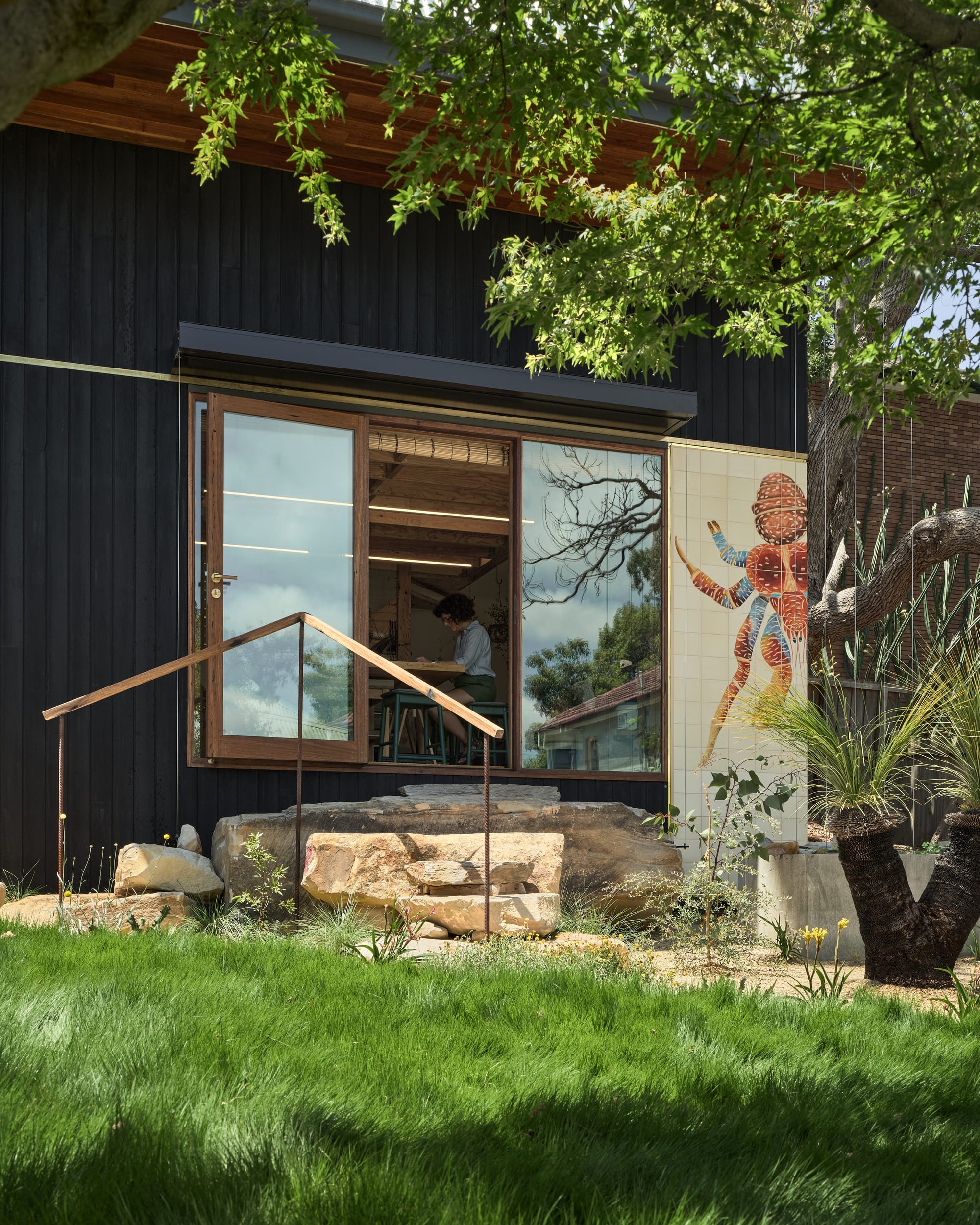 Coconut Crab by Alexander Symes Architect. Photography by Barton Taylor Photography. Dark timber clad structure with glass timber doors opening onto stone steps. Long green grass in foreground.