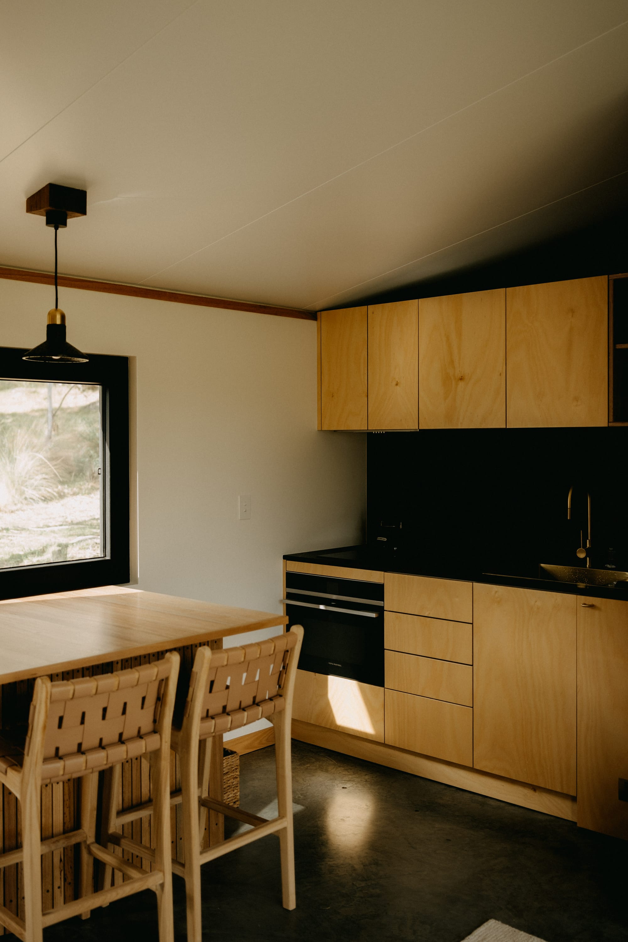 Crafters Eco-Cabins. Image copyright of Crafters. Raw plywood veneer kitchen cabinetry and dining table. Polished concrete floors, white walls and slanted white ceiling.