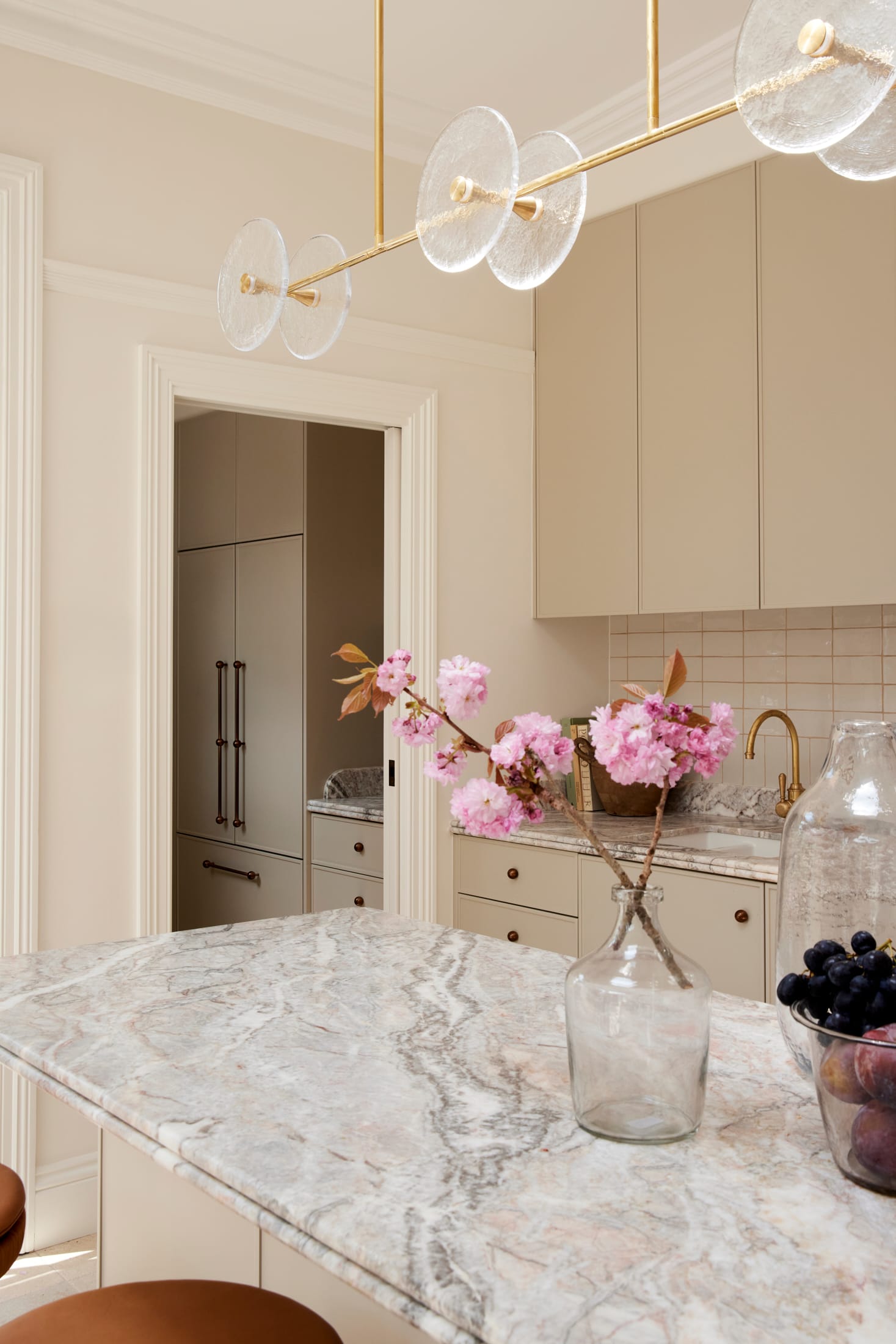 Drummoyne House by studio BARBARA. Photography by Jacqui Turk. Marble benchtop in kitchen with tiled splashback. Beige cabinetry. Gold and glass pendant light.