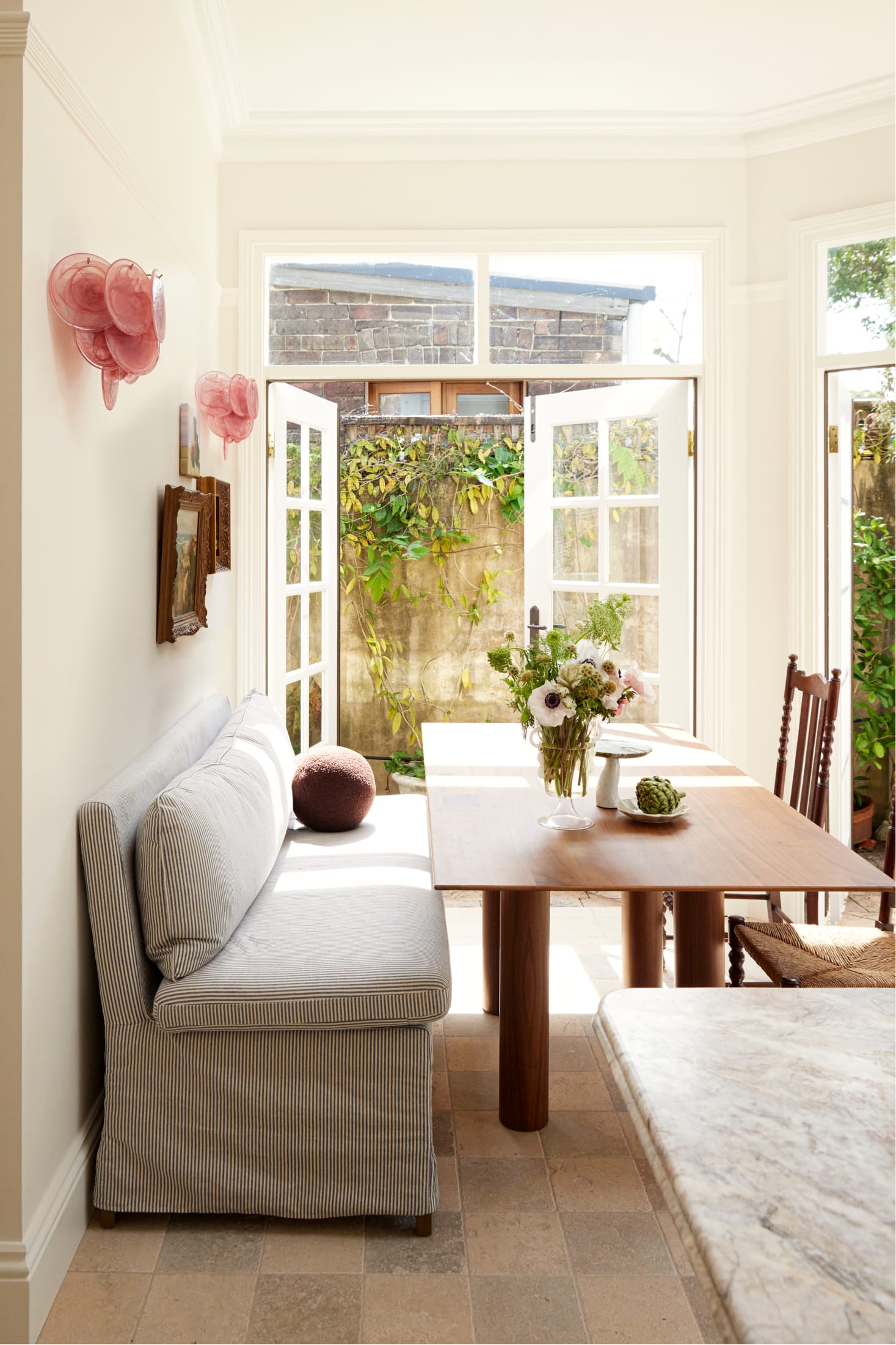 Drummoyne House by studio BARBARA. Photography by Jacqui Turk. Breakfast nook with checkered travertine flooring. Striped bench seat alongside timber dining table. French doors open onto terrace garden.