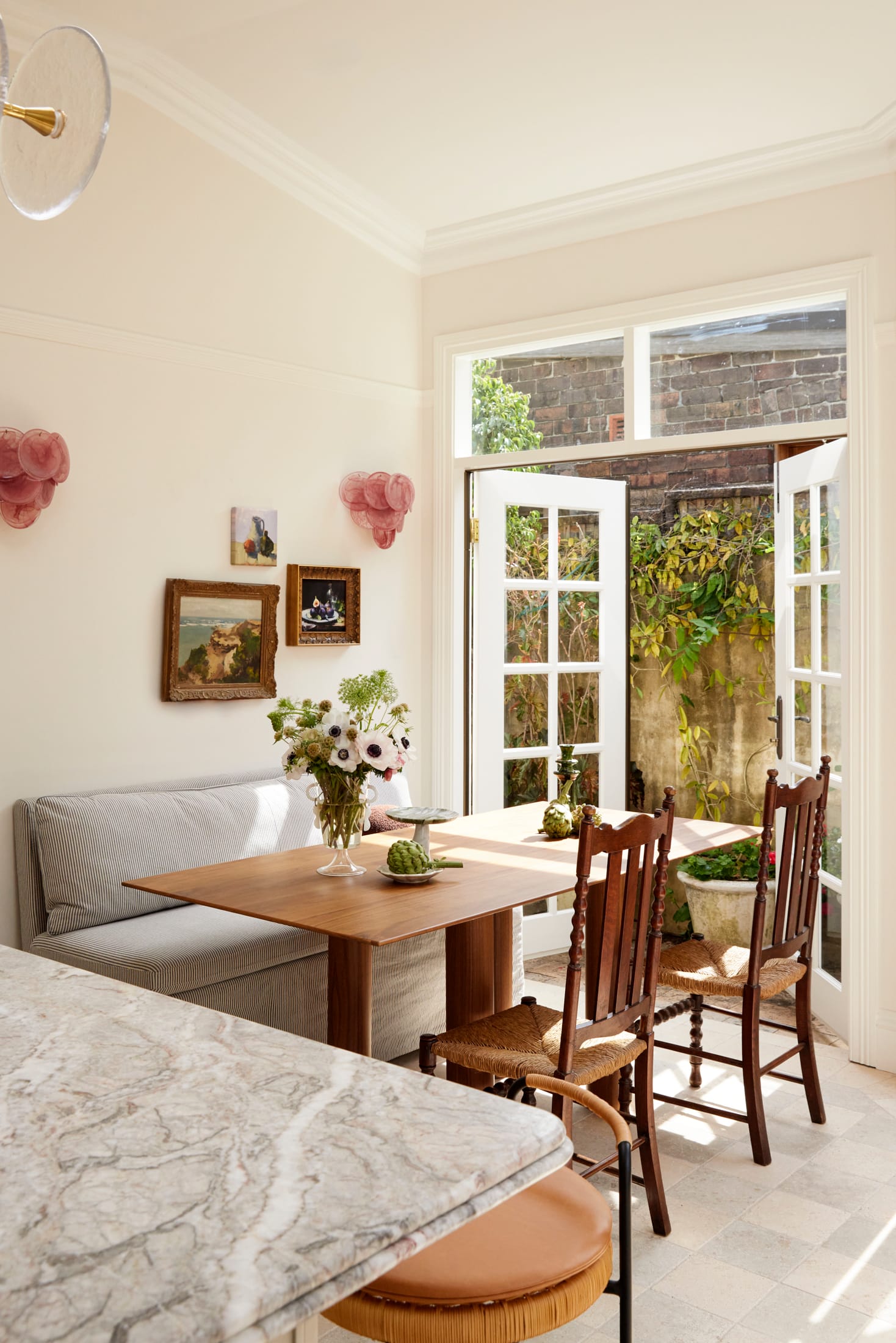 Drummoyne House by studio BARBARA. Photography by Jacqui Turk. Breakfast nook with built-in striped benchseat and timber dining table. Heritage timber dining chairs. Views onto green terrace garden.