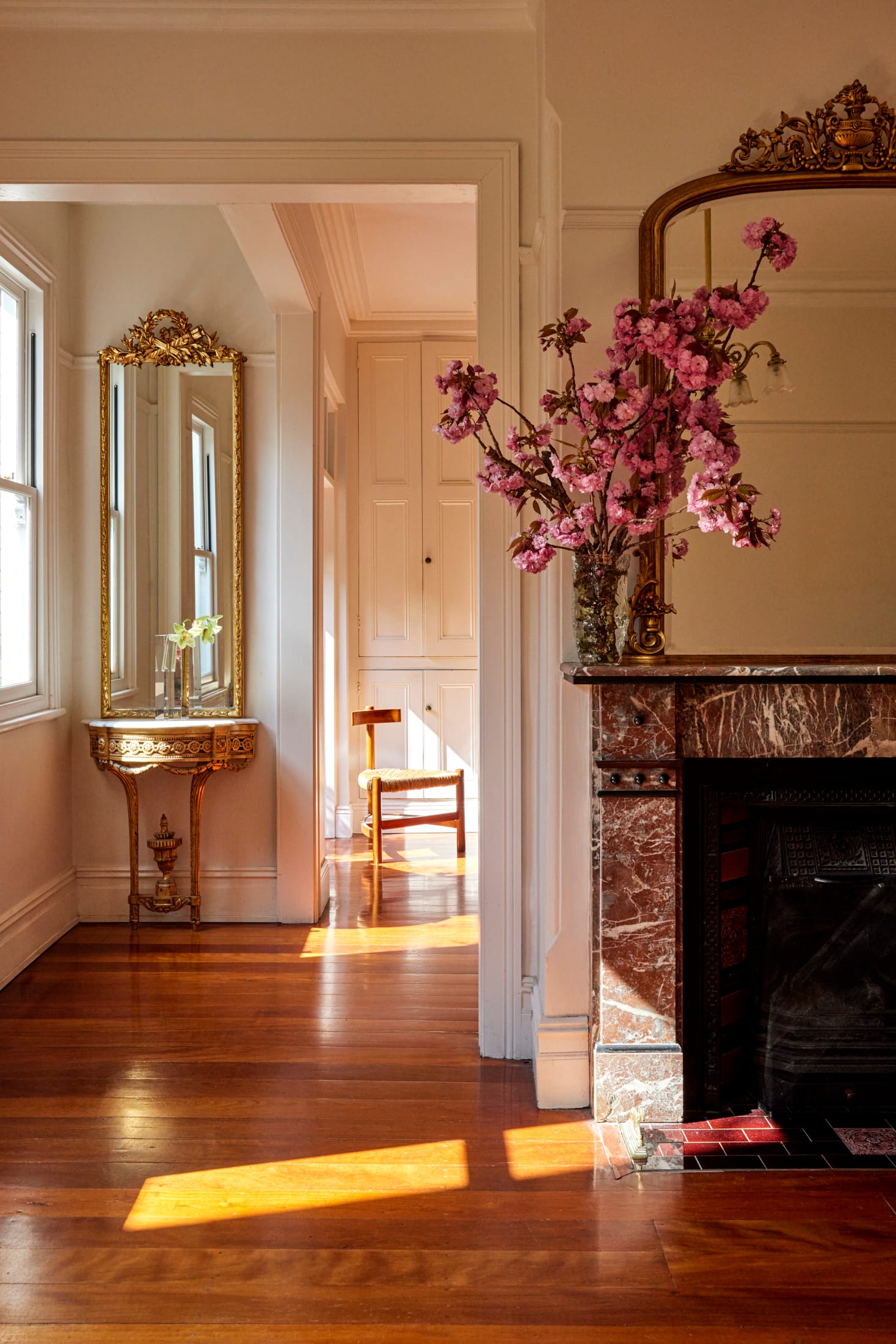 Drummoyne House by studio BARBARA. Photography by Jacqui Turk. Heritage marble fireplace with ornate gold framed mirror. Hardwood floors. Vintage ornate, gold mirror and sideboard in background.