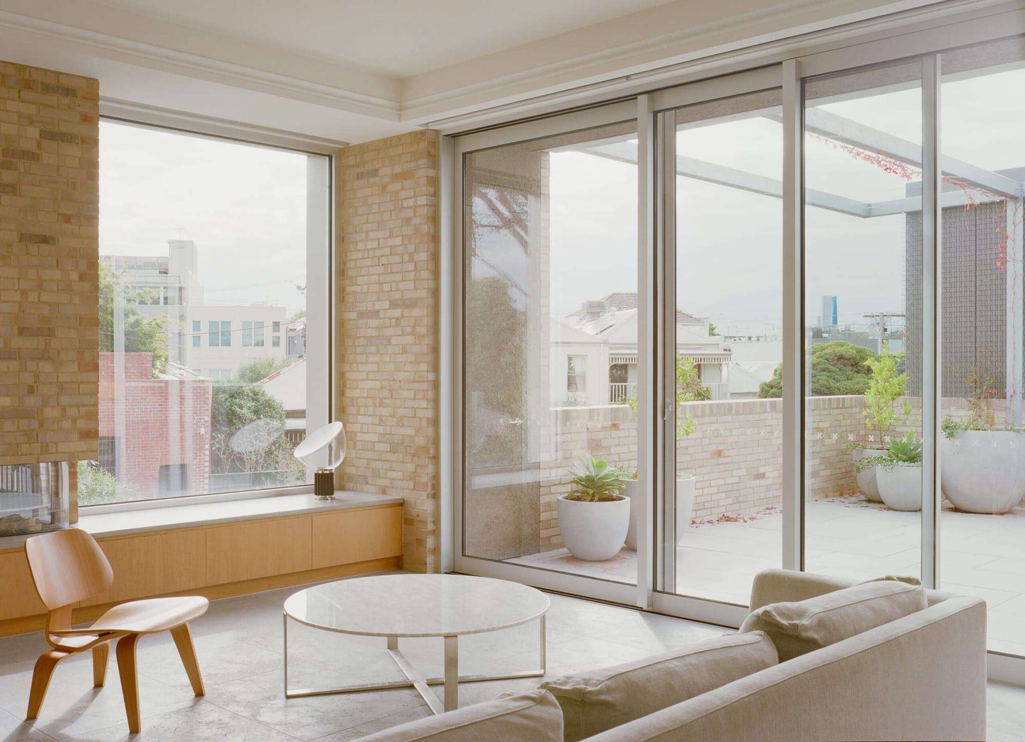 Esplanade House by Eckersley Architects. Photography by Pier Carthew. Living space with full length folding doors, light brick walls and concrete floor tiles. Timber cabinetry and seating. 