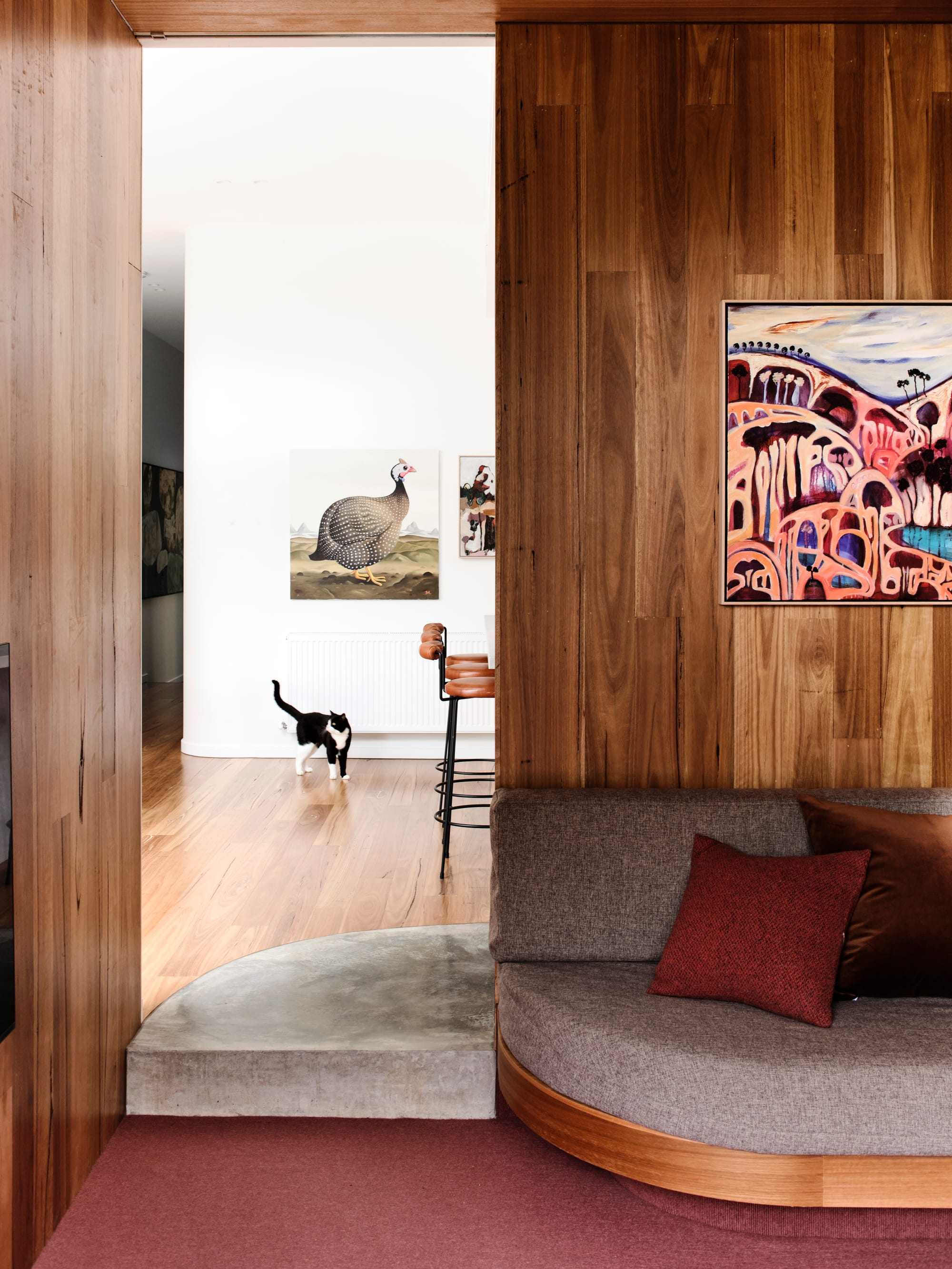 Fitzroy North Residence. Photography by Dean Bradley. Sunken living space with curved timber and grey integrated seating. Concrete step down into living space and timber walls.