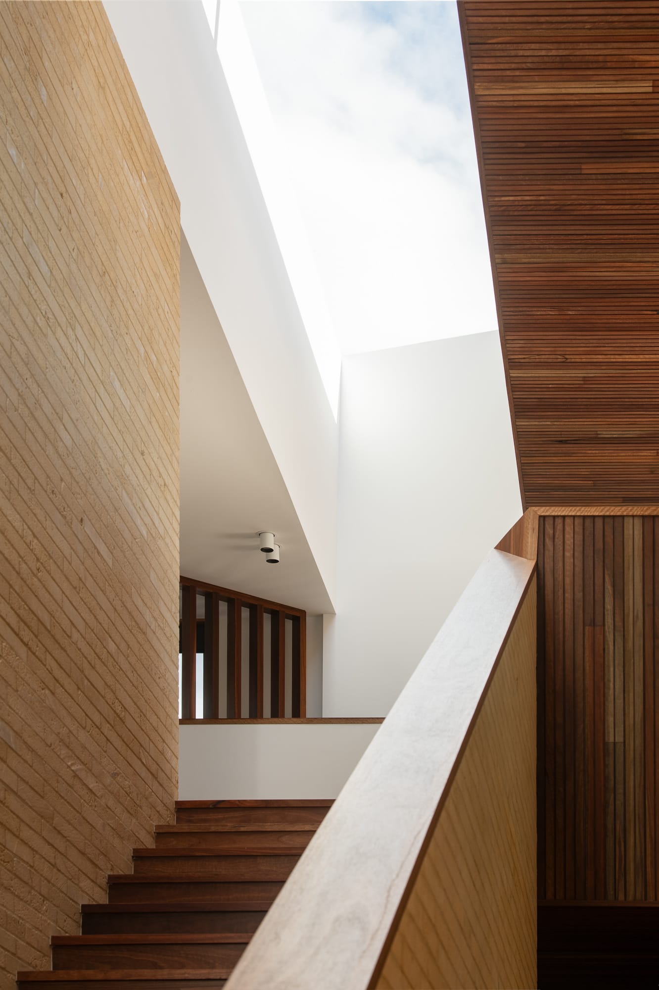 Mortlock Timber Series: The Milldam. Photography by Anjie Blair. Light brick and dark timber staircase with large overhead void and skylight in white ceiling. 