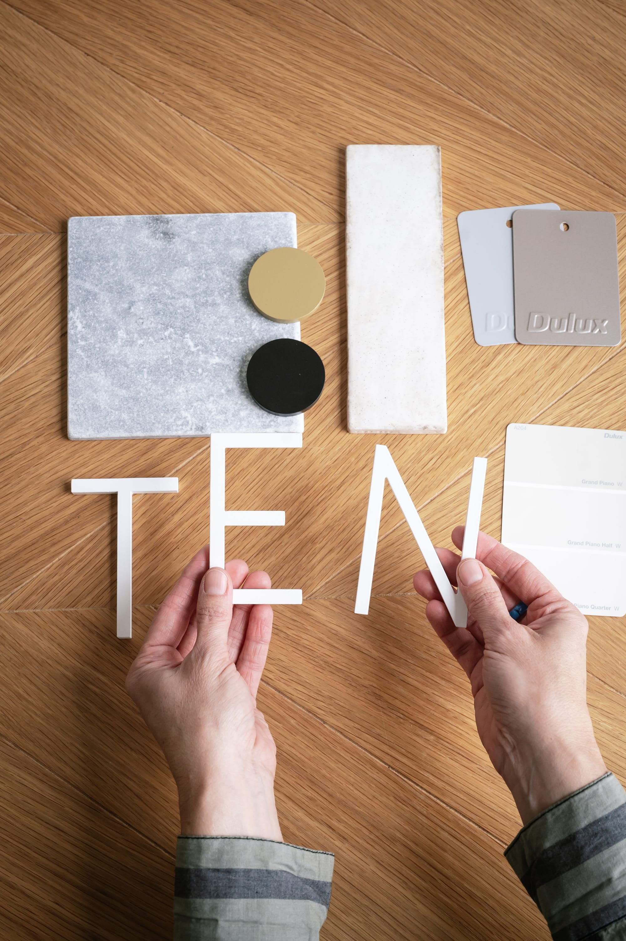 Peninsula House Numbers. Image copyright of Peninsula House Numbers. White metal capital letters spelling out 'TEN'. Metal, stone and paint swatches in background.