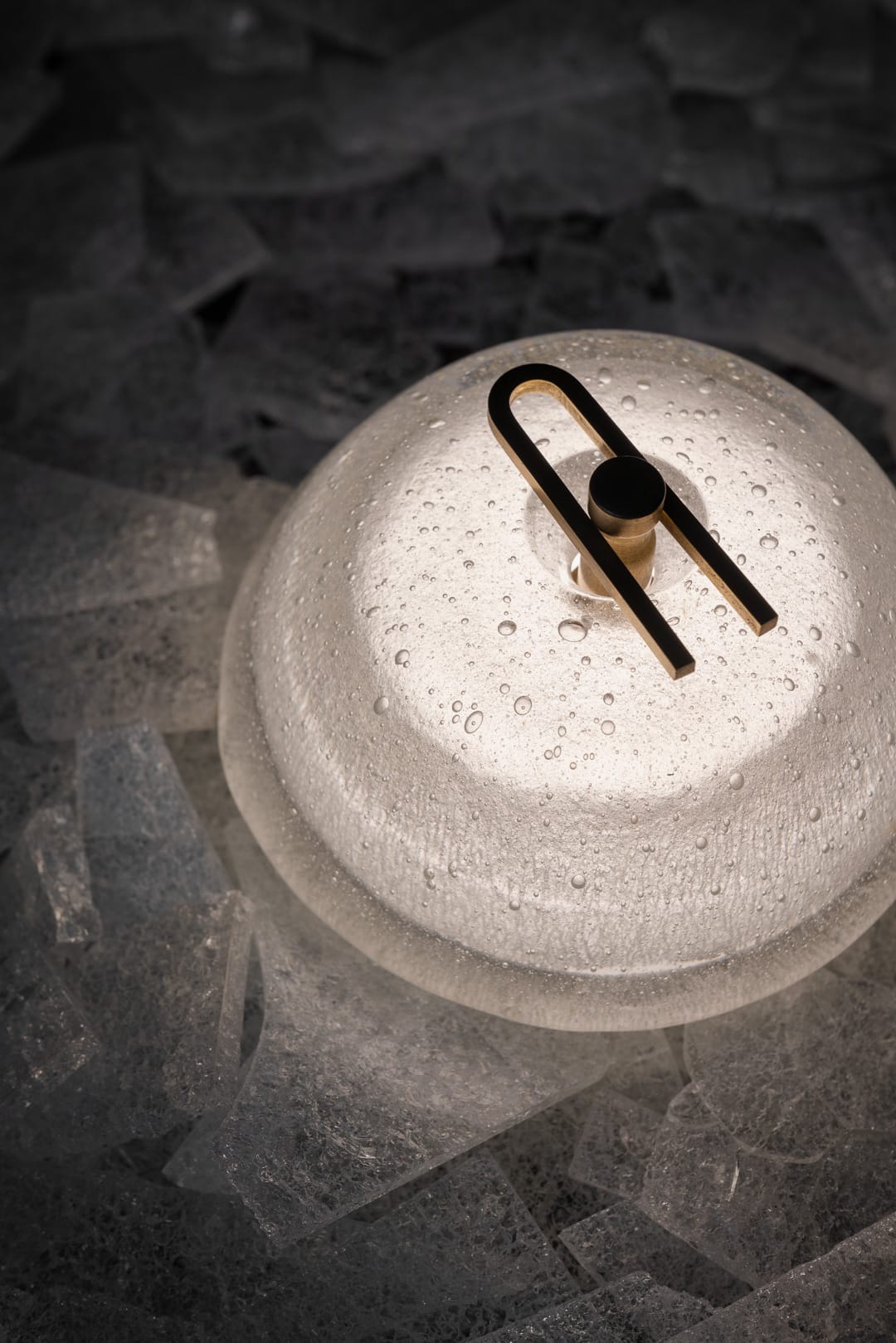 Point Five by South Drawn. Image copyright of South Drawn. Close up of domed light with bubbled texture and brass U-pin sitting on bed of crackled glass shards.