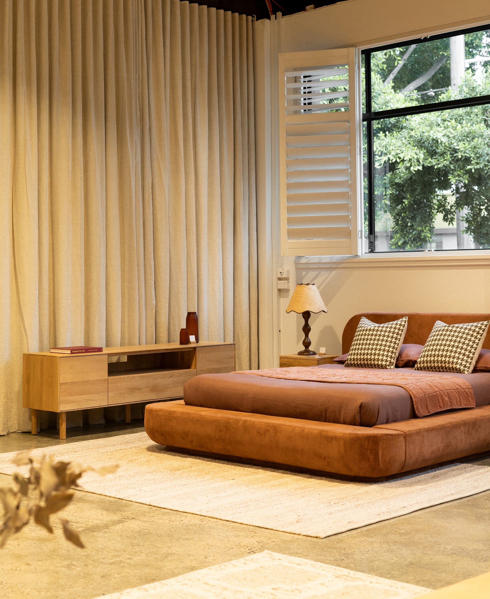 RJ Living's New Sydney Retail Space. Photography by Nathan Oakley. Tan suede bed frame with maroon linen. Jute floor rug and timber sideboard.