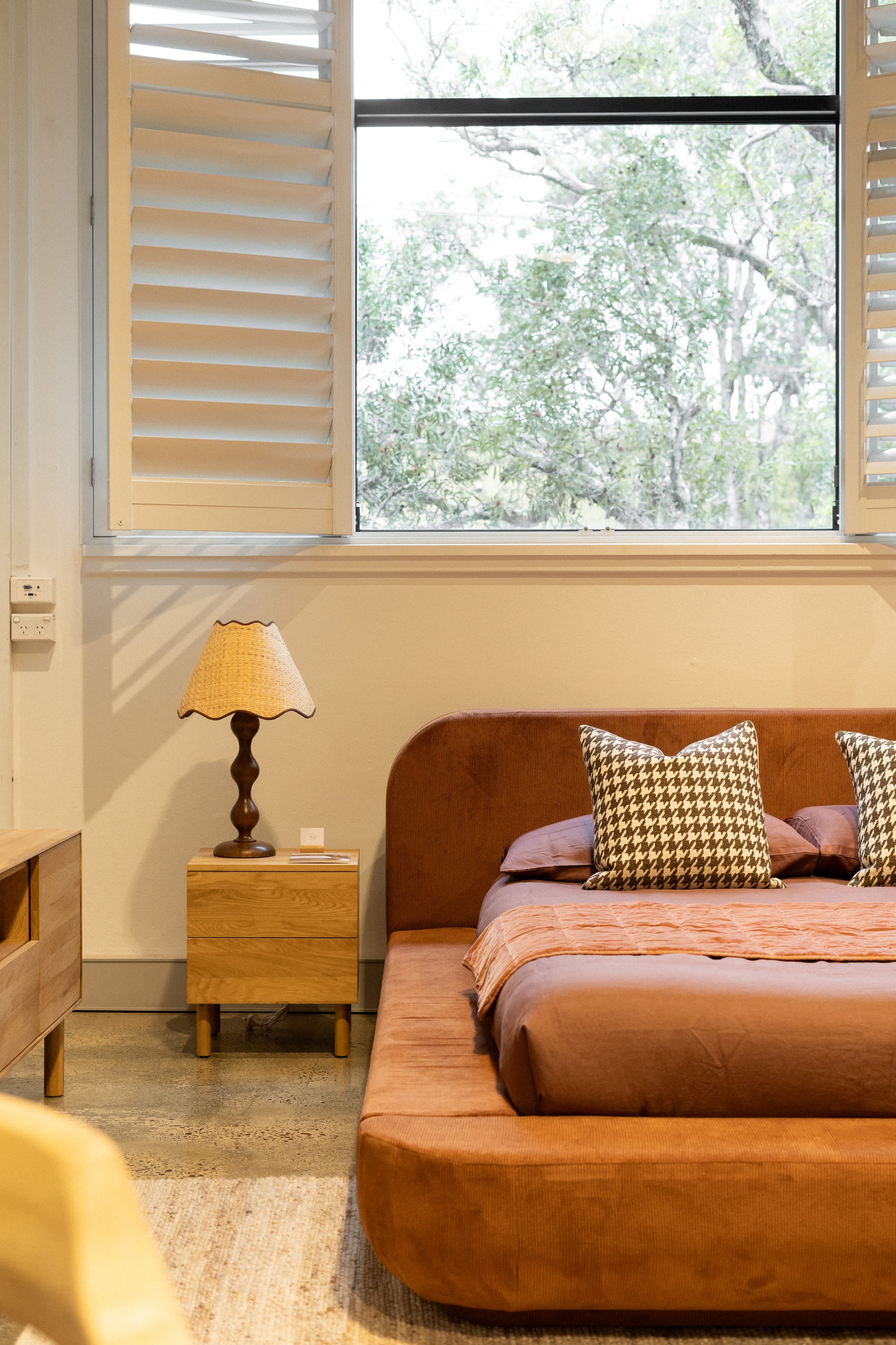 RJ Living's New Sydney Retail Space. Photography by Nathan Oakley. Tan material bedframe with matching linen. Timber bedside table and sideboard. White walls and polished concrete floors. 