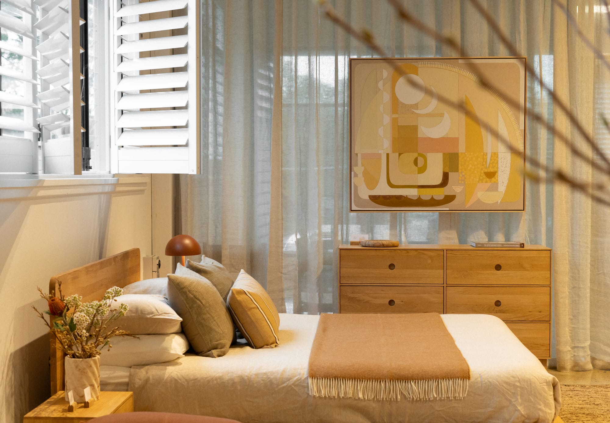 RJ Living's New Sydney Retail Space. Photography by Nathan Oakley. Bedroom space with white linen bedding and timber bedframe. Timber dresser and abstract wall art. Sheer curtains.