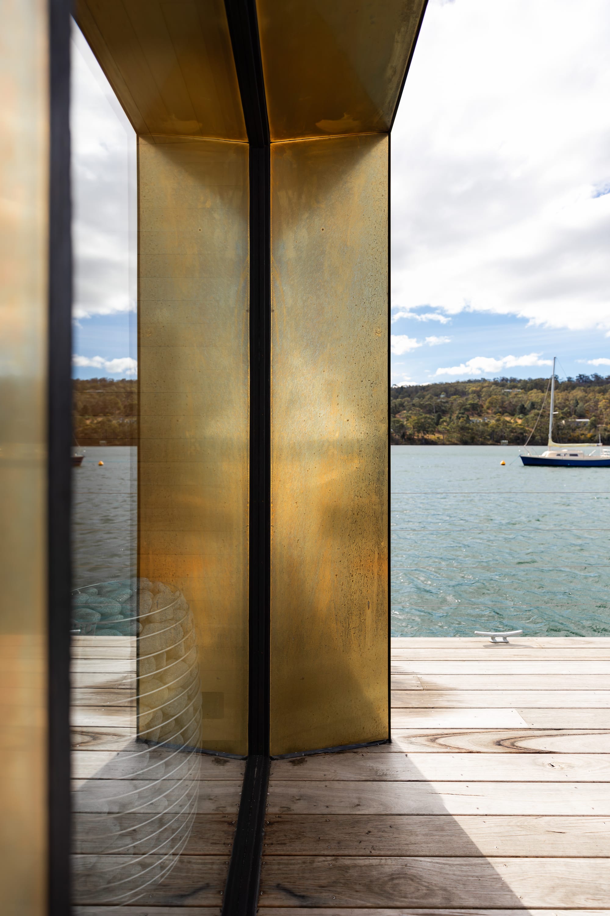 Sauna Boat Tasmania. Photography by Natasha Mulhall. Bronze metal wrap on sauna boat exterior wall. Timber decking. Glazed window. 