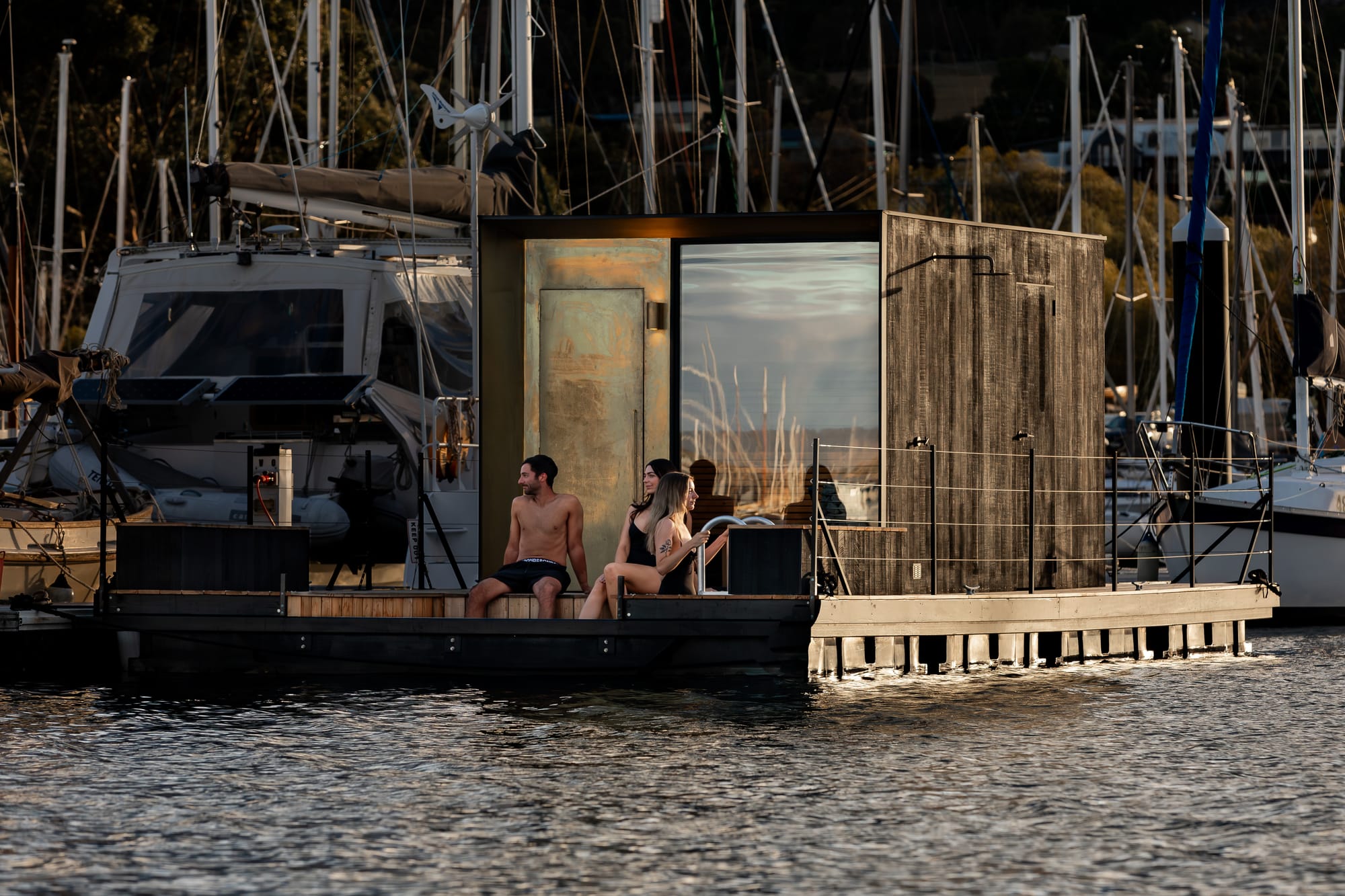 Sauna Boat Tasmania. Photography by Natasha Mulhall. Three adults using outdoor pool attached to sauna boat. Boat in harbour surrounded by other boats. 