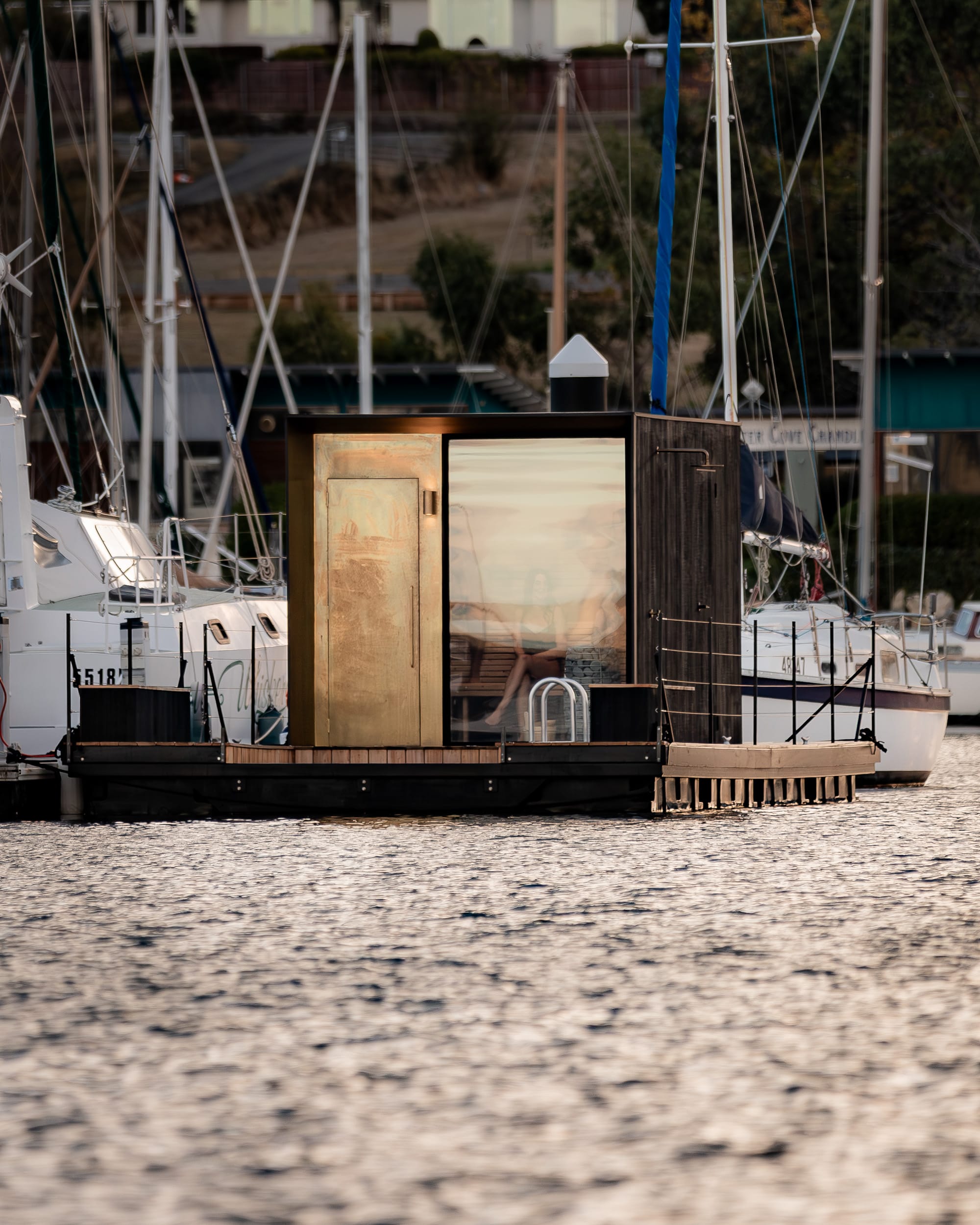Sauna Boat Tasmania. Photography by Natasha Mulhall. Saunt boat on water, surrounded by other boats in harbour. 