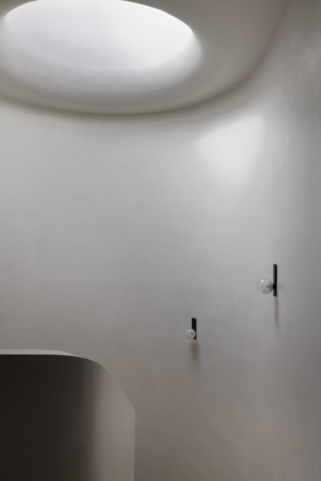 An interior shot from the top of the stair showing the curved rendered wall with wall lights and a feature round skylight above with sun coming through