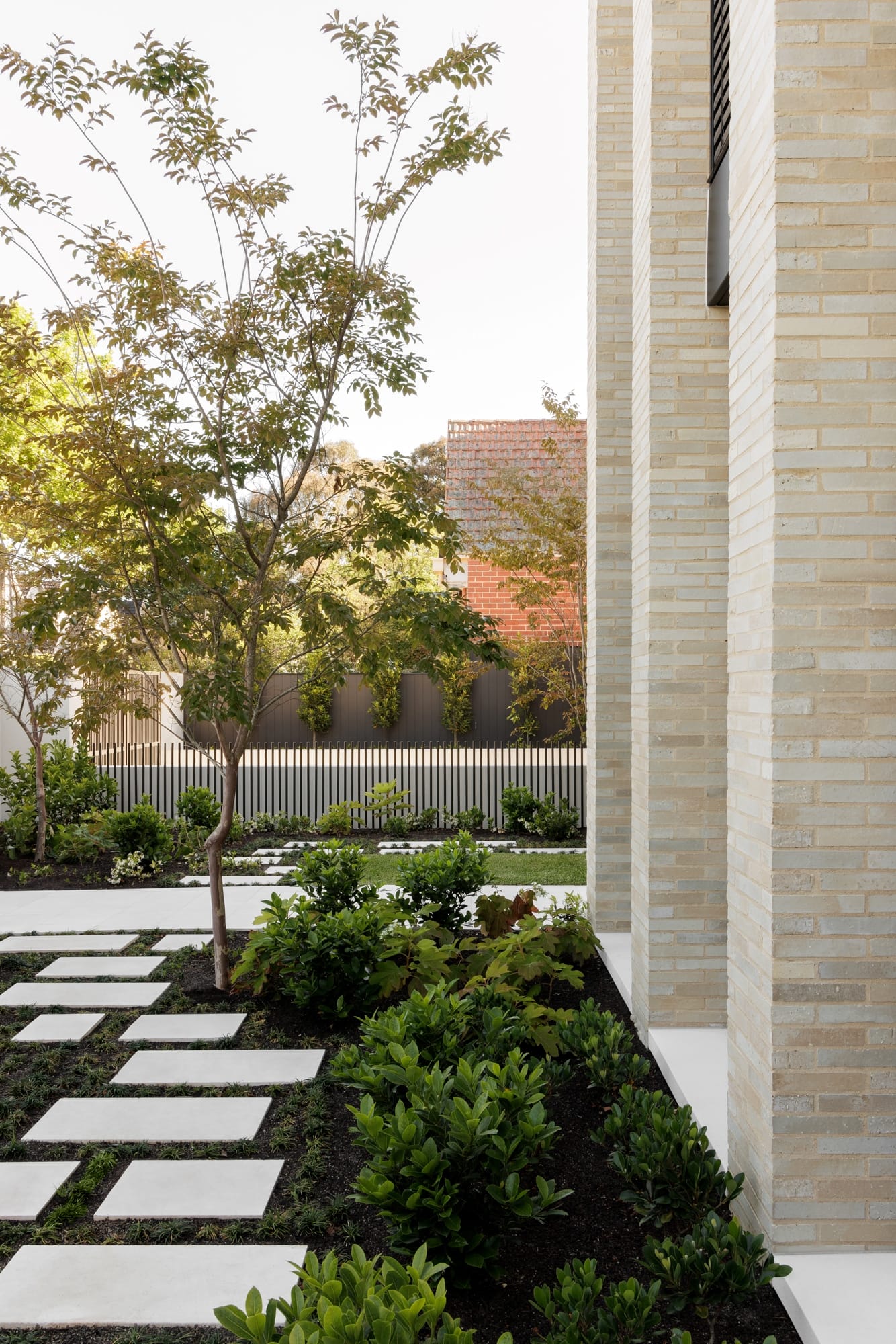An exterior shot showing the landscape against the blonde brickwork of the house and a steel fence in the background