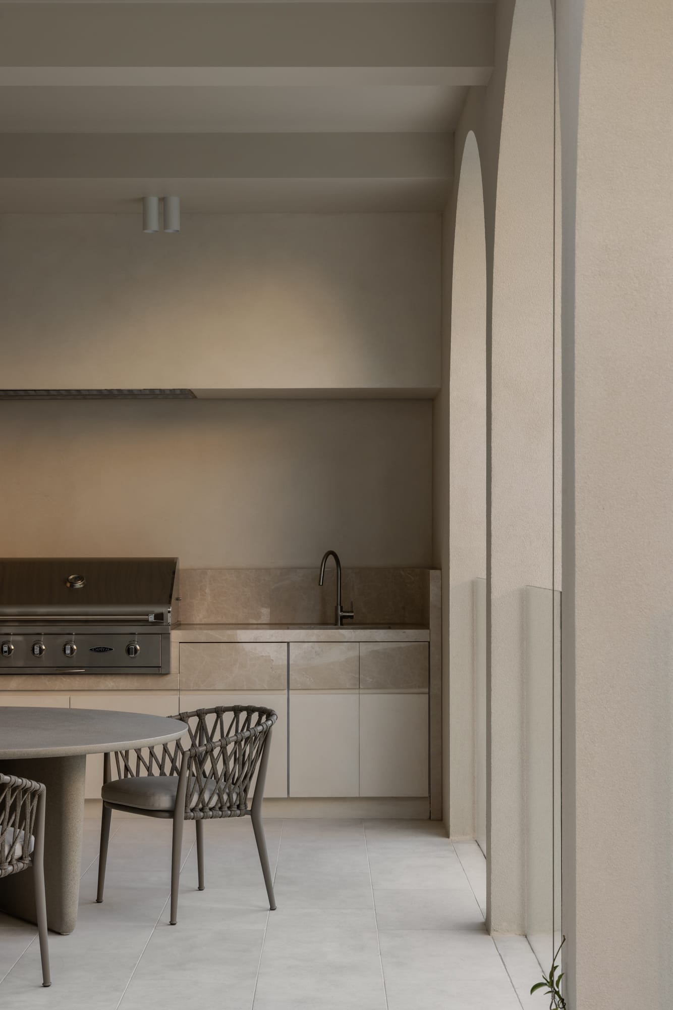 An external view of the covered courtyard bbq area with a built in bbq and a sink in the outdoor workspace. Dining setting to the left of the image.