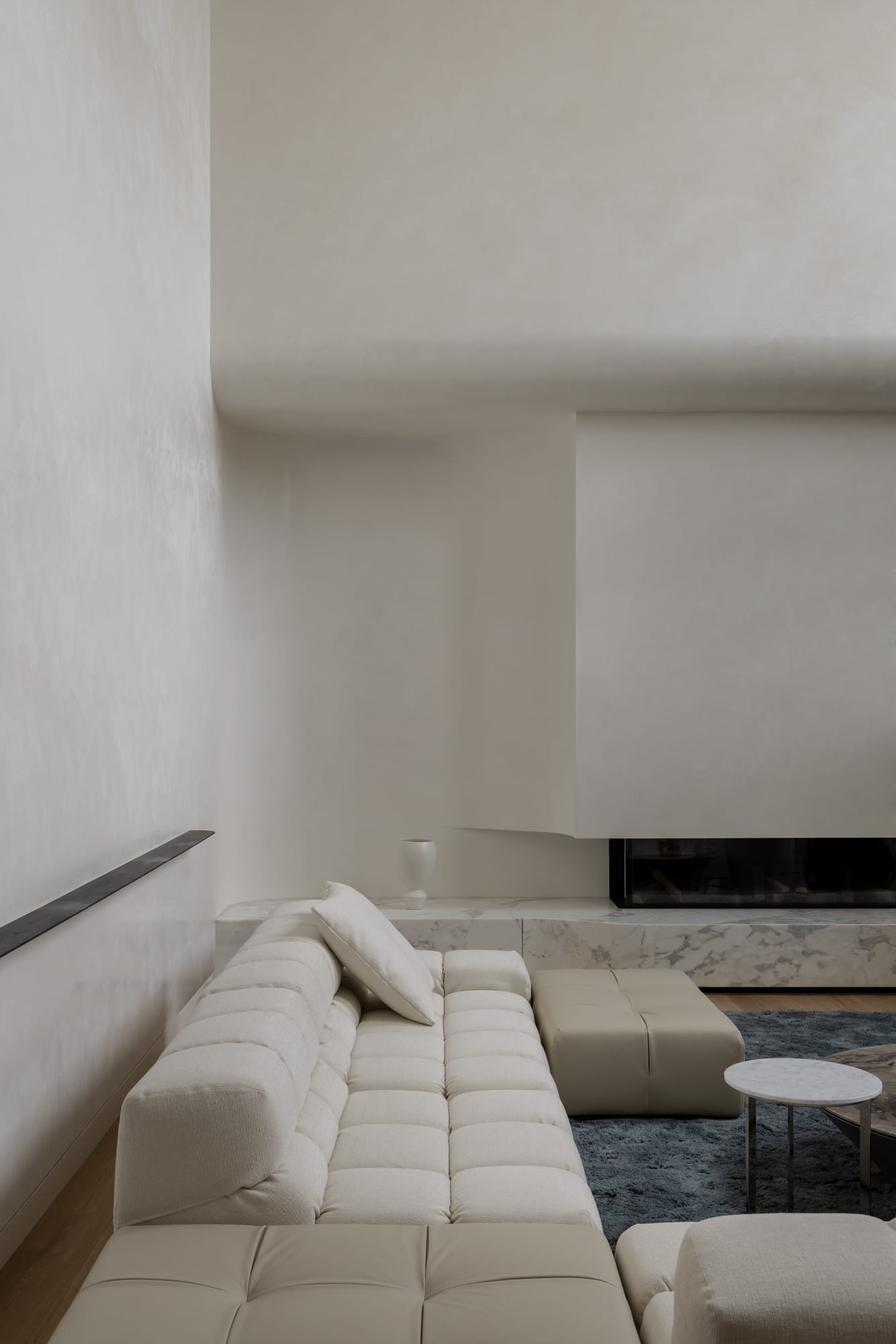 An interior shot of the well styled living room with a designer sofa, blue rug and a feature fireplace that has a marble bench