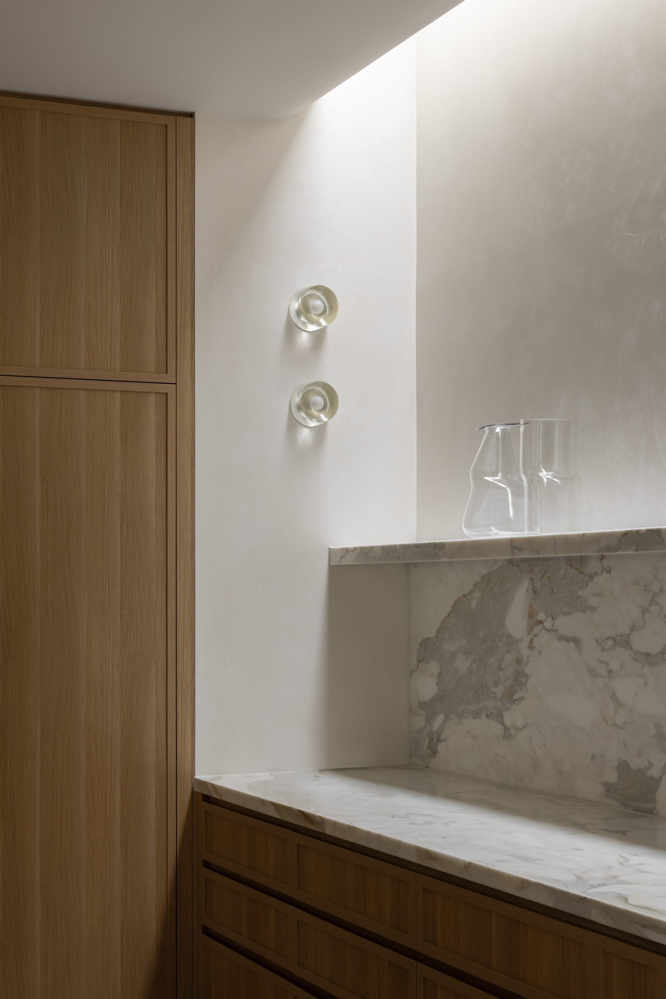 A detail shot of the kitchen showing the white marble benchtop, backsplash and shelf with timber joinery and two feature wall lights