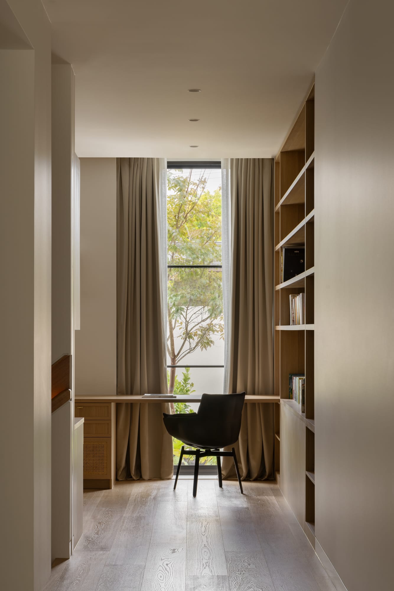 An interior shot of a home office showing a designer chair at a timber deck with a view out to the garden and timber storage to the right