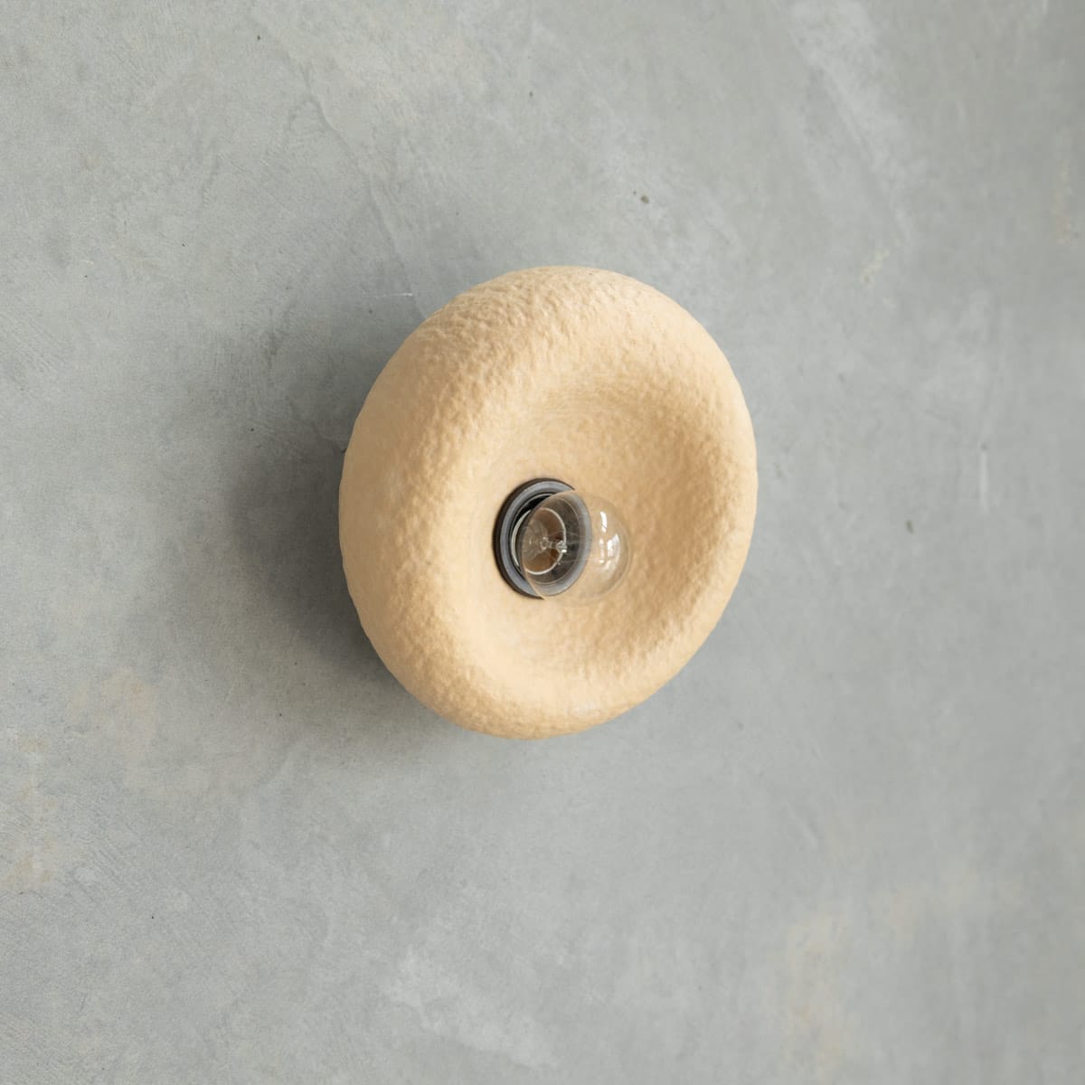 Pumice Sconce in Sand. Image copyright of Crete Studio. Yellow textured abstract wall sconce on grey concrete wall.