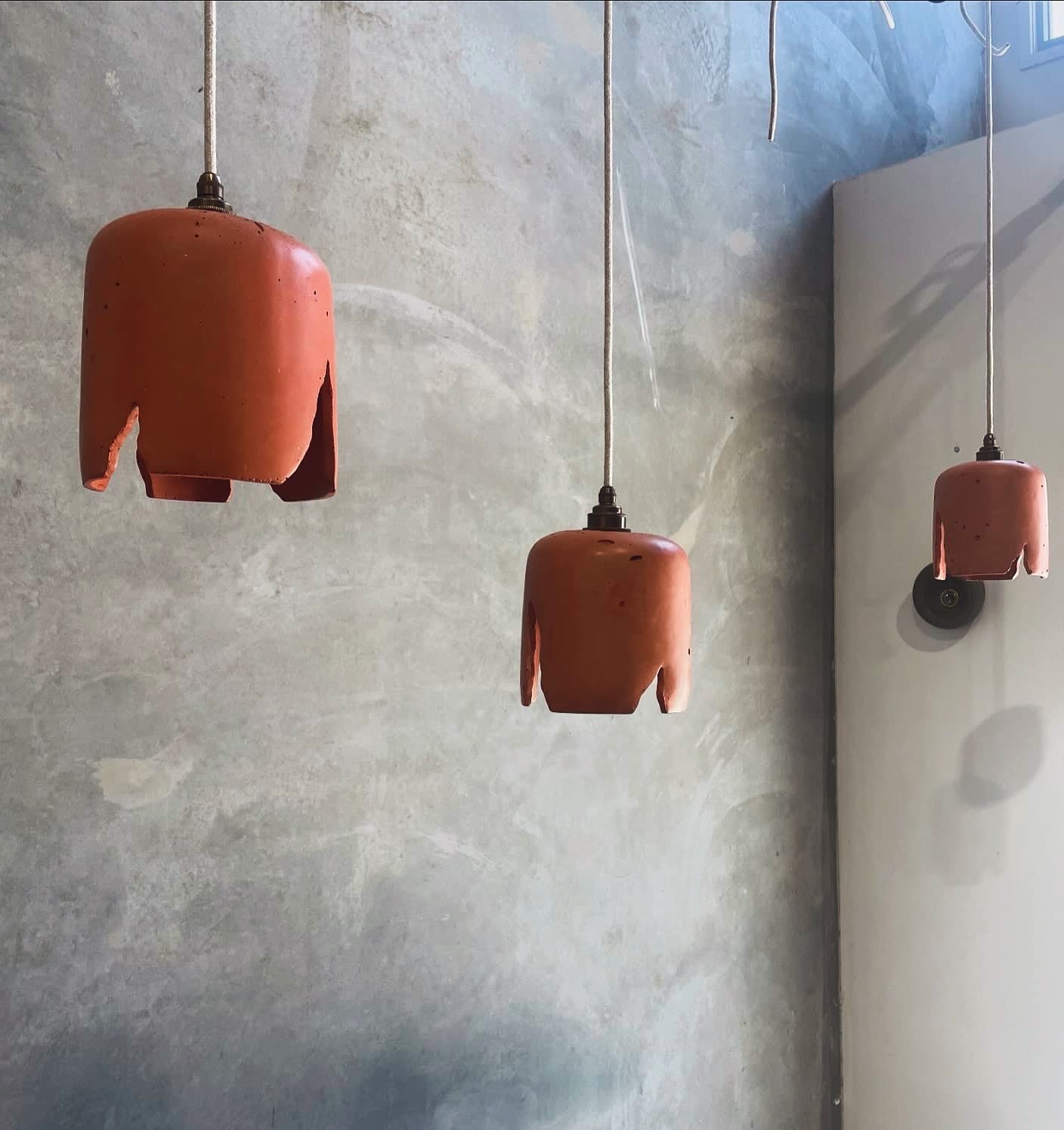 Wattle Pendants in Terracotta. Image copyright of Crete Studio. Three burnt orange colored concrete pendant lights hanging on front of concrete wall.