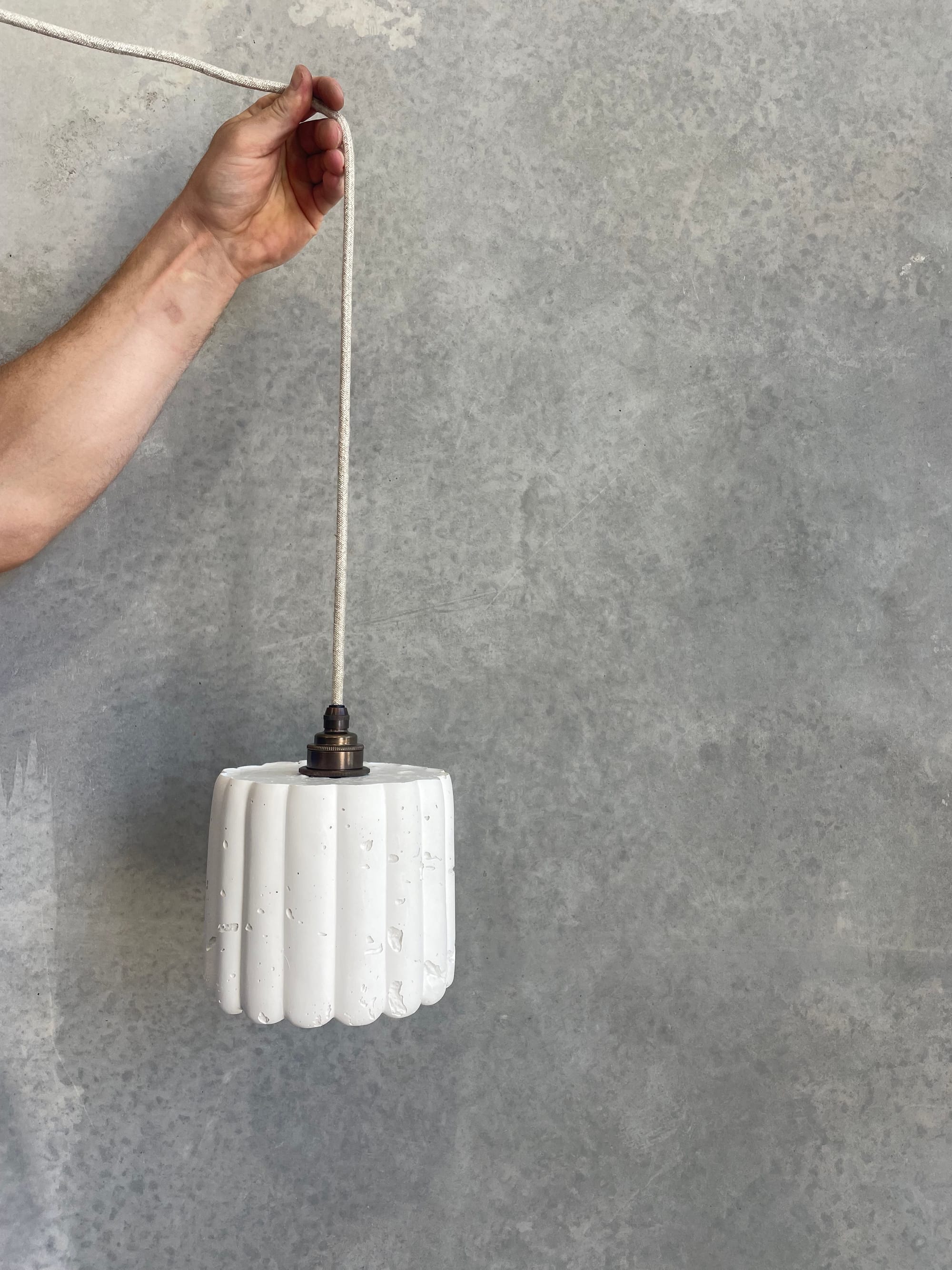 Crete Studio. Image copyright of Crete Studio. Hand holding white scalloped light fixture in front of concrete wall.