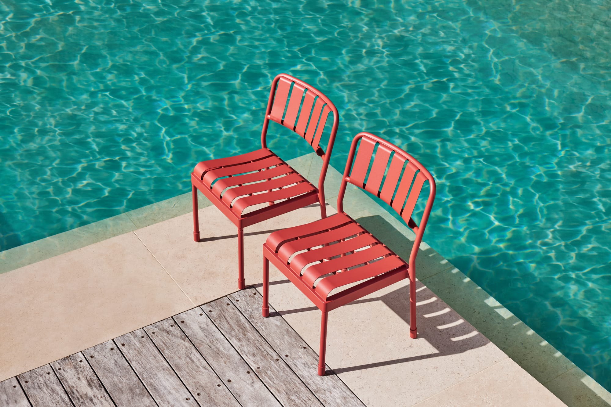 Torakina Outdoor Dining Seating in Outback Rose. Two pink metal chairs sitting by a blue pool.