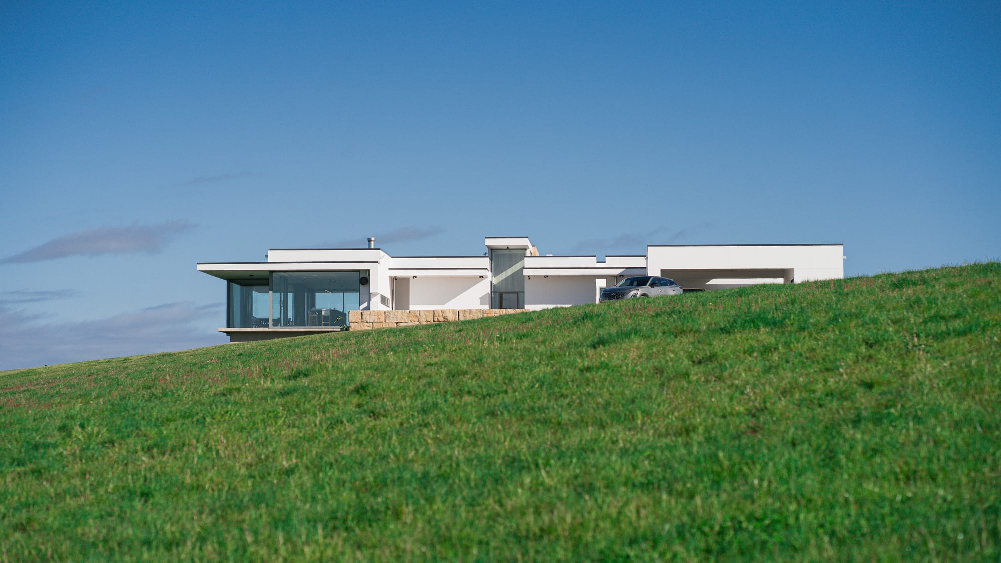 The Cloud at Sen Vineyard. Photography by Ben Little. Enclosed courtyard area with white gravel and firepit to left of contemporary white home at night, with warm light visible through full length glass walls. 