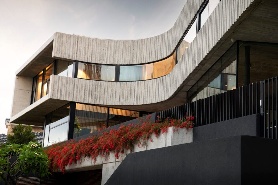 Truro Residence by Hillam Architects. Photography by Joel Barbitta. Low angle of multi-level residential home with concrete finish, curved facade and red cascading foliage on black retaining wall. 