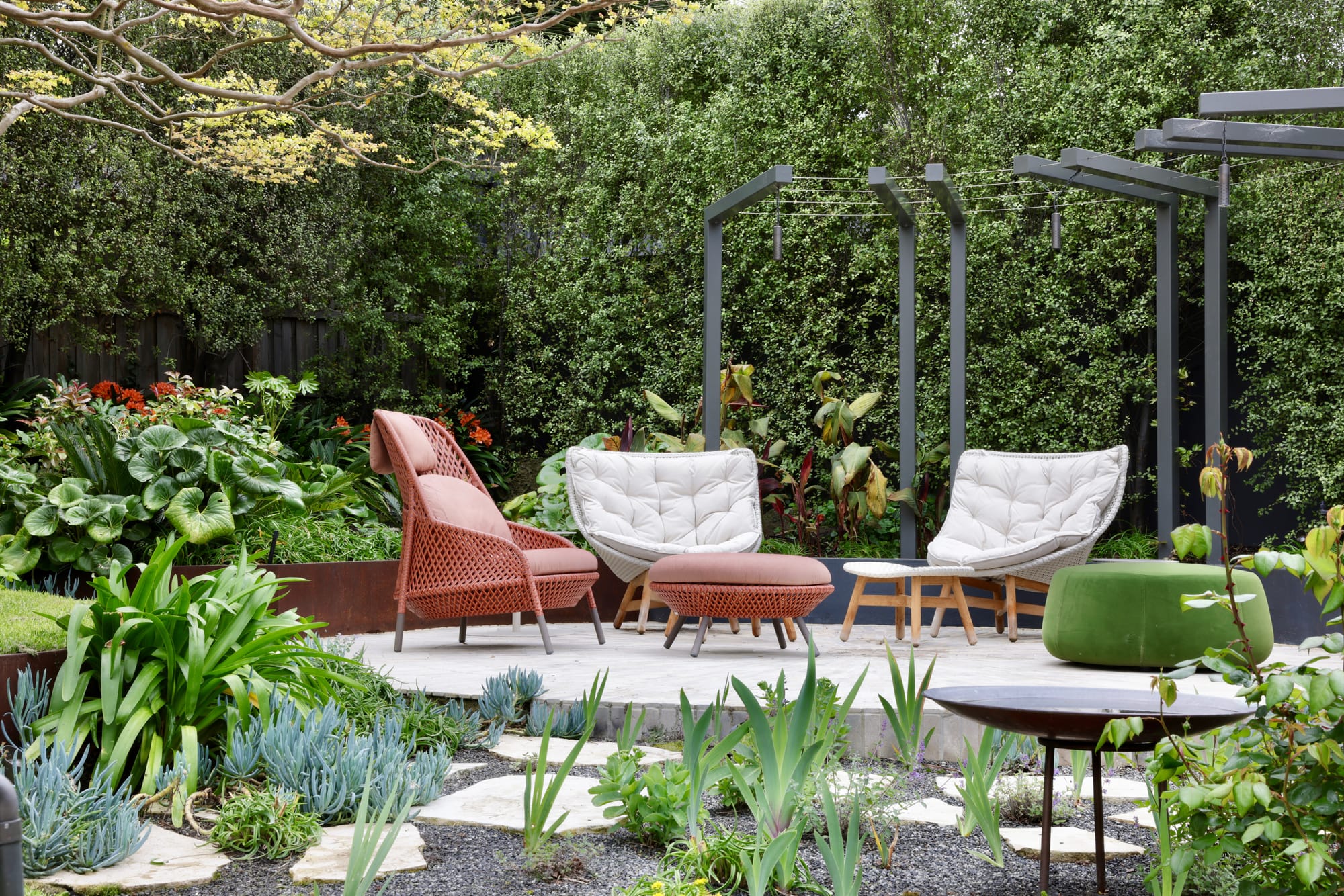 Glen Iris by Julie Crowe Landscape Design x Cosh Living. Photography by&nbsp;Eloise Sim. Three outdoor armchairs in red and white and a green ottoman arranged on grey paved circular seating area in outdoor garden. 