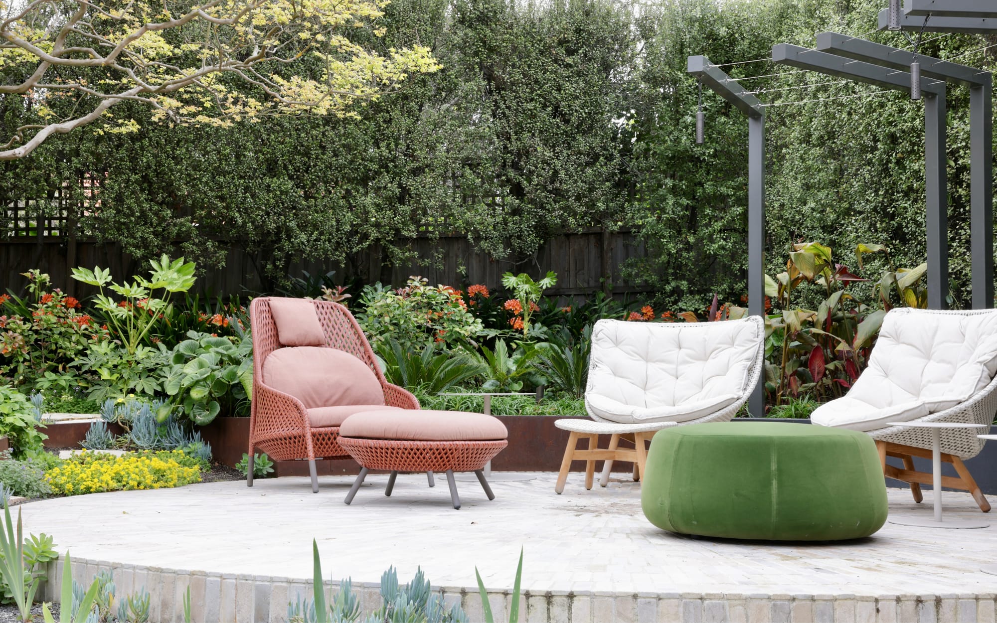 Glen Iris by Julie Crowe Landscape Design x Cosh Living. Photography by Eloise Sim. White armchair and matching footstool in outdoor garden, with tall wall of green foliage in backdrop. 