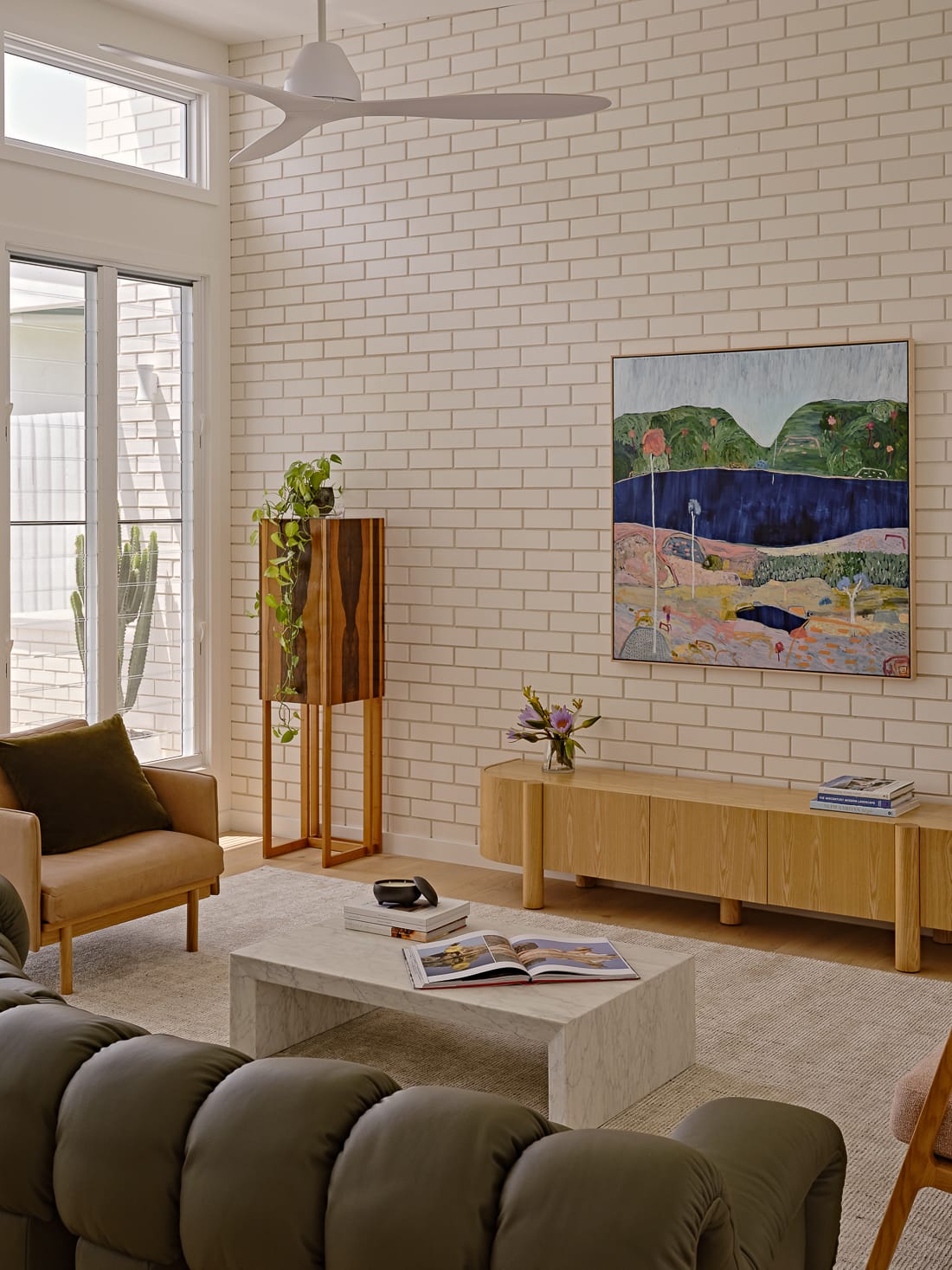 Twin Palms House by FURNISHD. Photography by Brock Beazley. Living space with tufted green leather couch, marble coffee table, timber side board, abstract wall art and white brick walls.