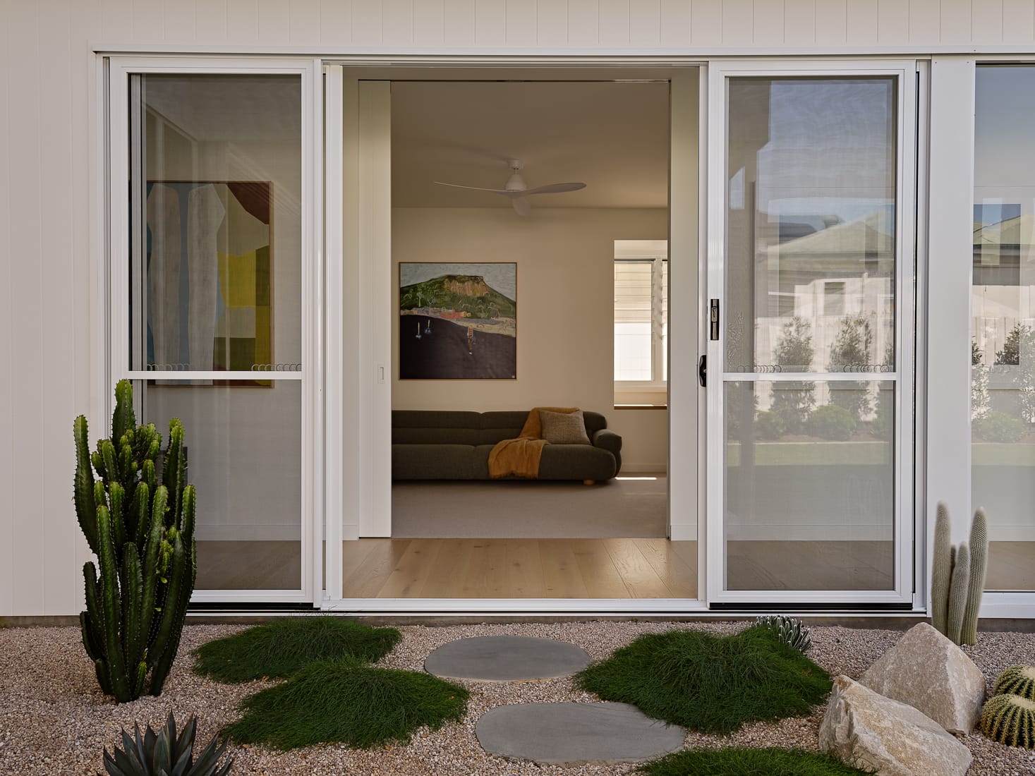 Twin Palms House by FURNISHD. Photography by Brock Beazley. Courtyard garden with crushed stone, rocks, cacti, round pavers and moss. Full length glass sliding door opening onto hallway and living space.