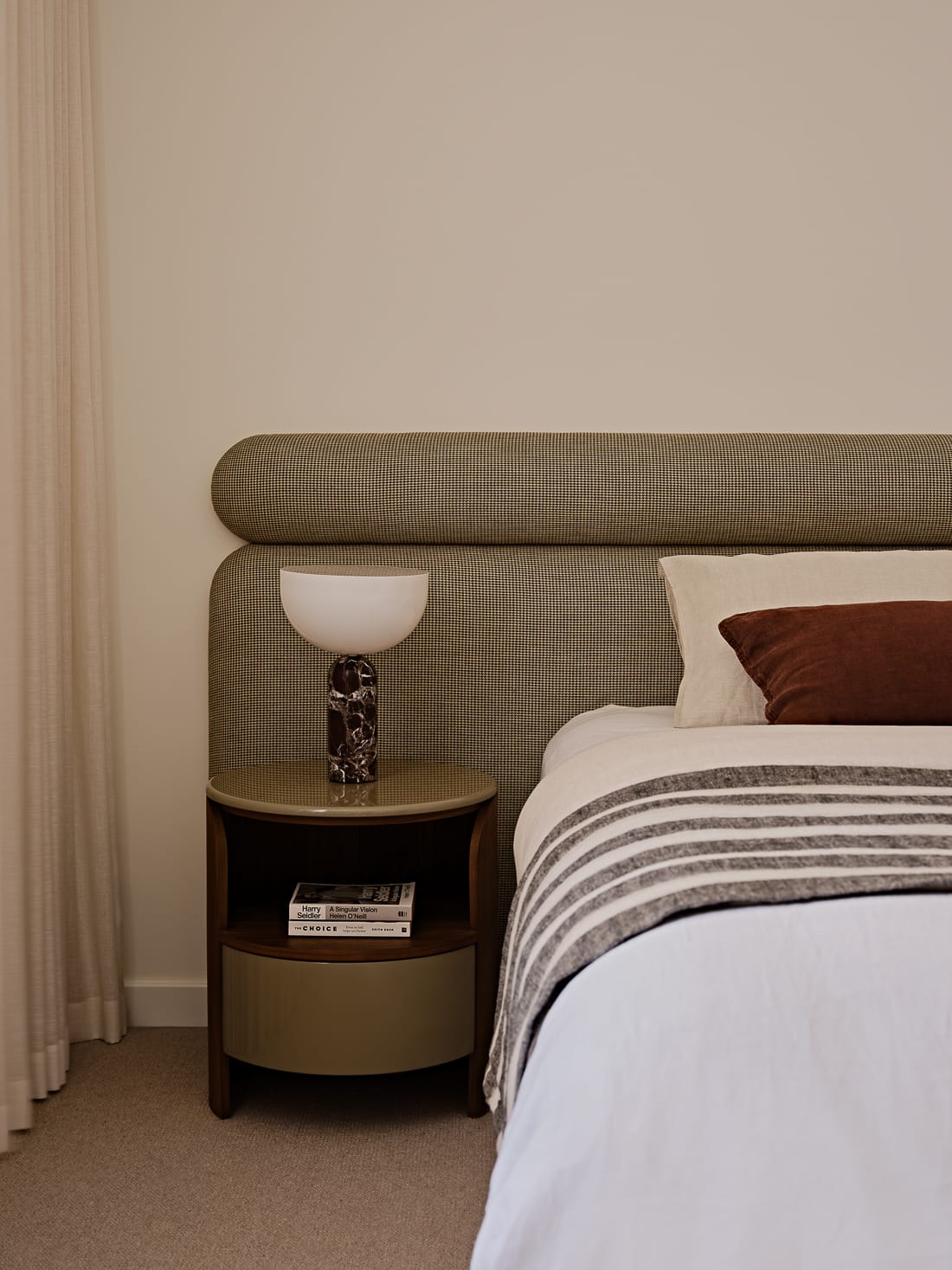 Twin Palms House by FURNISHD. Photography by Brock Beazley. Bedroom with upholstered fabric headboard in green houndstooth finish, white bed linen, striped throw rug, beige carpets and round timber bedside table. 