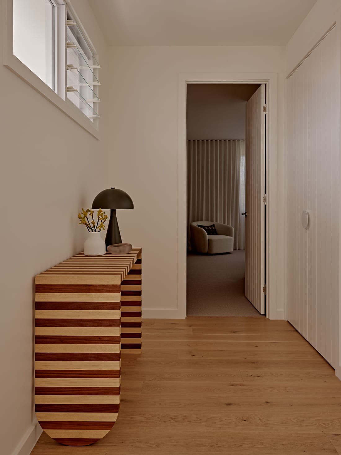 Twin Palms House by FURNISHD. Photography by Brock Beazley. Striped timber sideboard featuring light and warm timber, white timber clad walls in hallway to the right. 