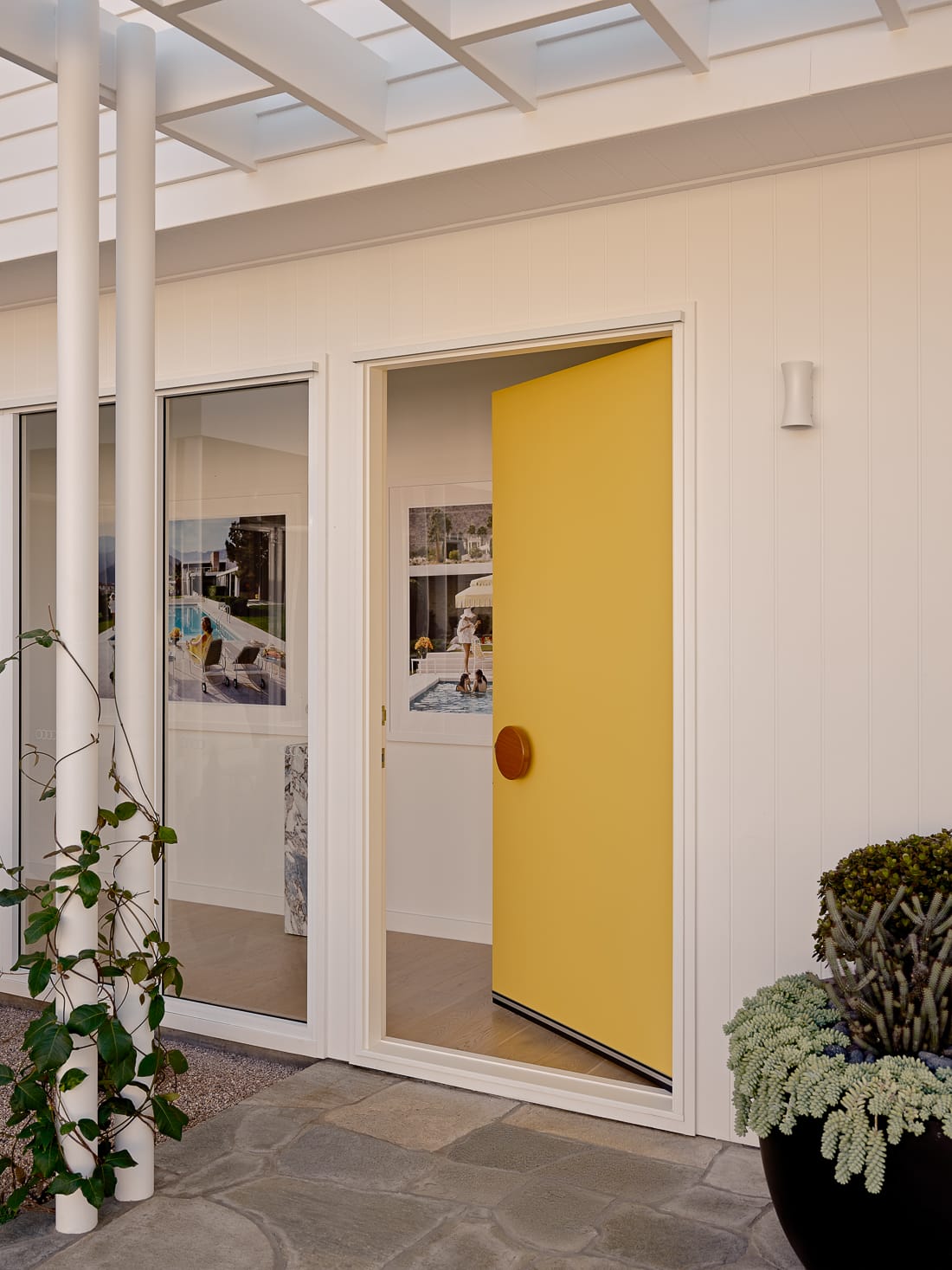 Twin Palms House by FURNISHD. Photography by Brock Beazley. Yellow door leading into timber hallway with matching wall art on white walls.