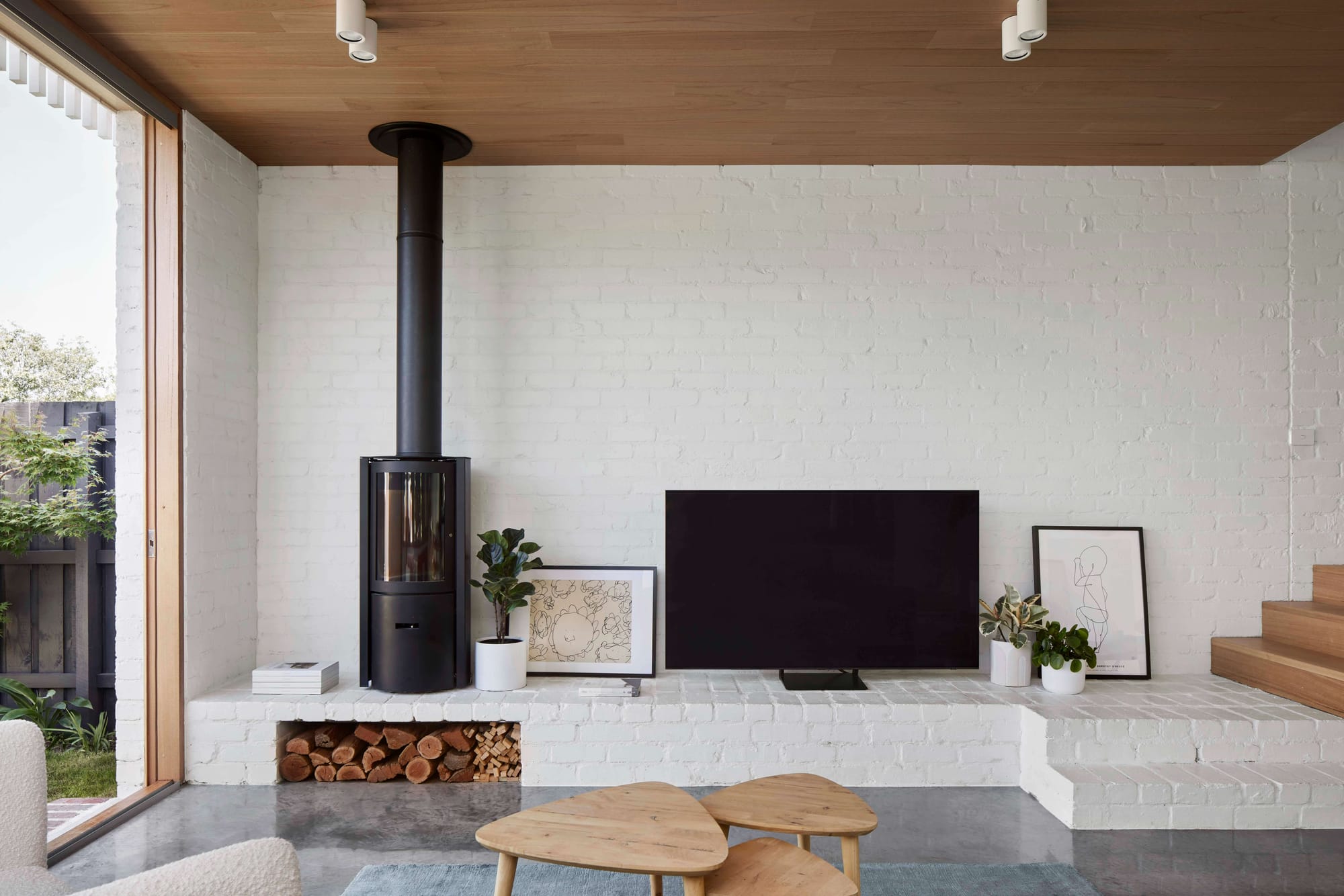 Ascot Vale House by Eckersley Architects. Photography by Tess Kelly. Living room space with white brick walls, fireplace, polished concrete floors and timber stairs and furnishings. 