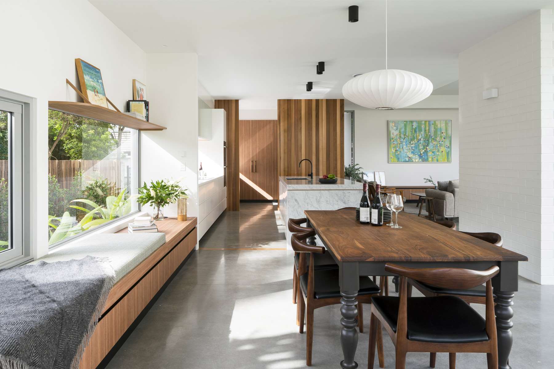 Auchenflower Courtyard House by Kelder Architects. Photography by Angus Martin Photography.  Open plan kitchen and dining space with polished concrete flooring, white brick walls, integrated window seating, timber dining table and lots of bright light coming through windows on left wall. 