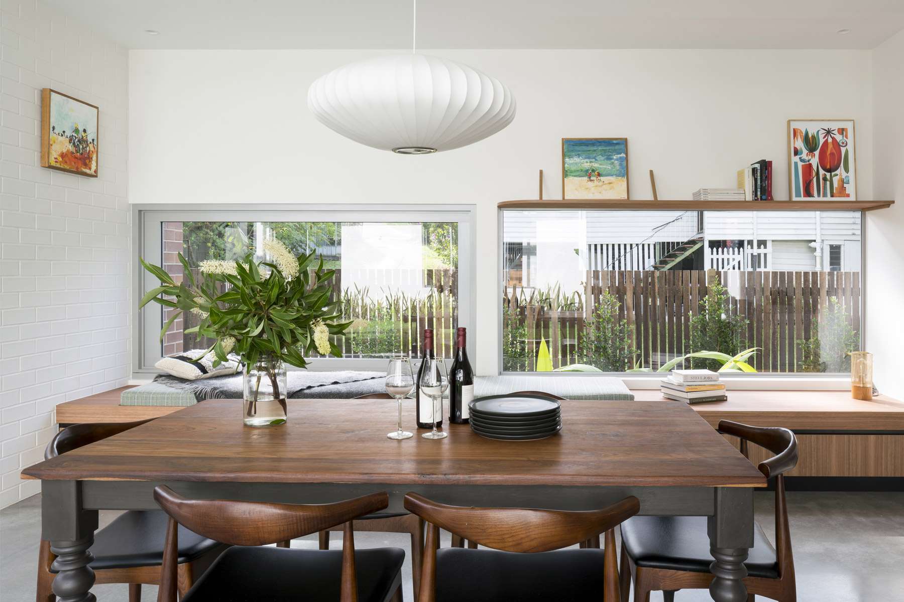 Auchenflower Courtyard House by Kelder Architects. Photography by Angus Martin Photography. Dining space with concrete floors, timber dining table, integrated window seating and bookshelves on white brick walls. 