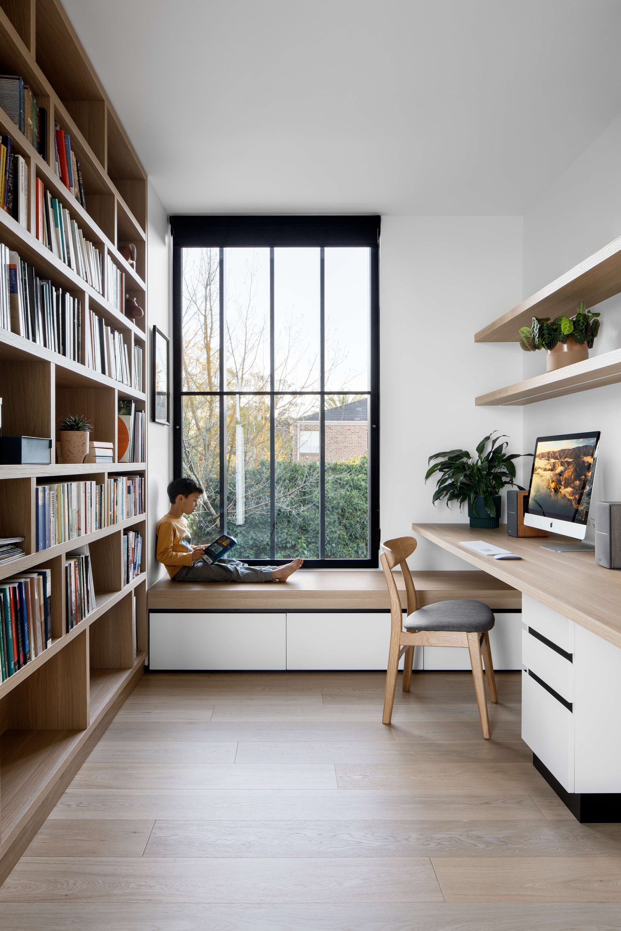 Dickens Residence by Chan Architecture. Photography by Tatjana Plitt. Study space with a young boy sitting on a timber integrated window seat reading a book. Space has timber flooring, integrated timber bookshelf and desk. 