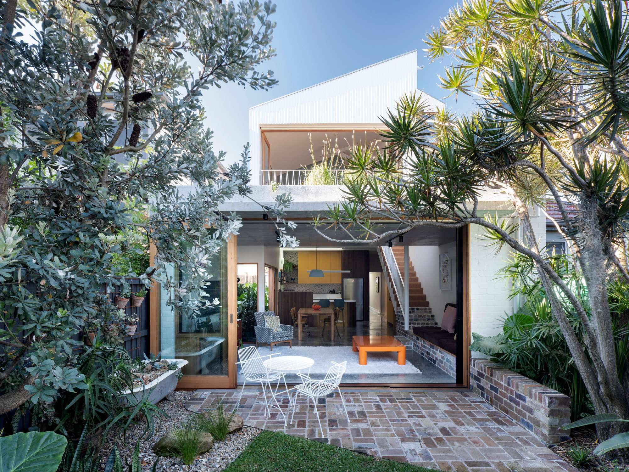 Fondue House by Castlepeake Architecture. Photography by Tom Ferguson. Rear facade of double storey home with full height timber sliding doors joining open plan kitchen, living and dining space with reclaimed brick paver outdoor entertaining area. 