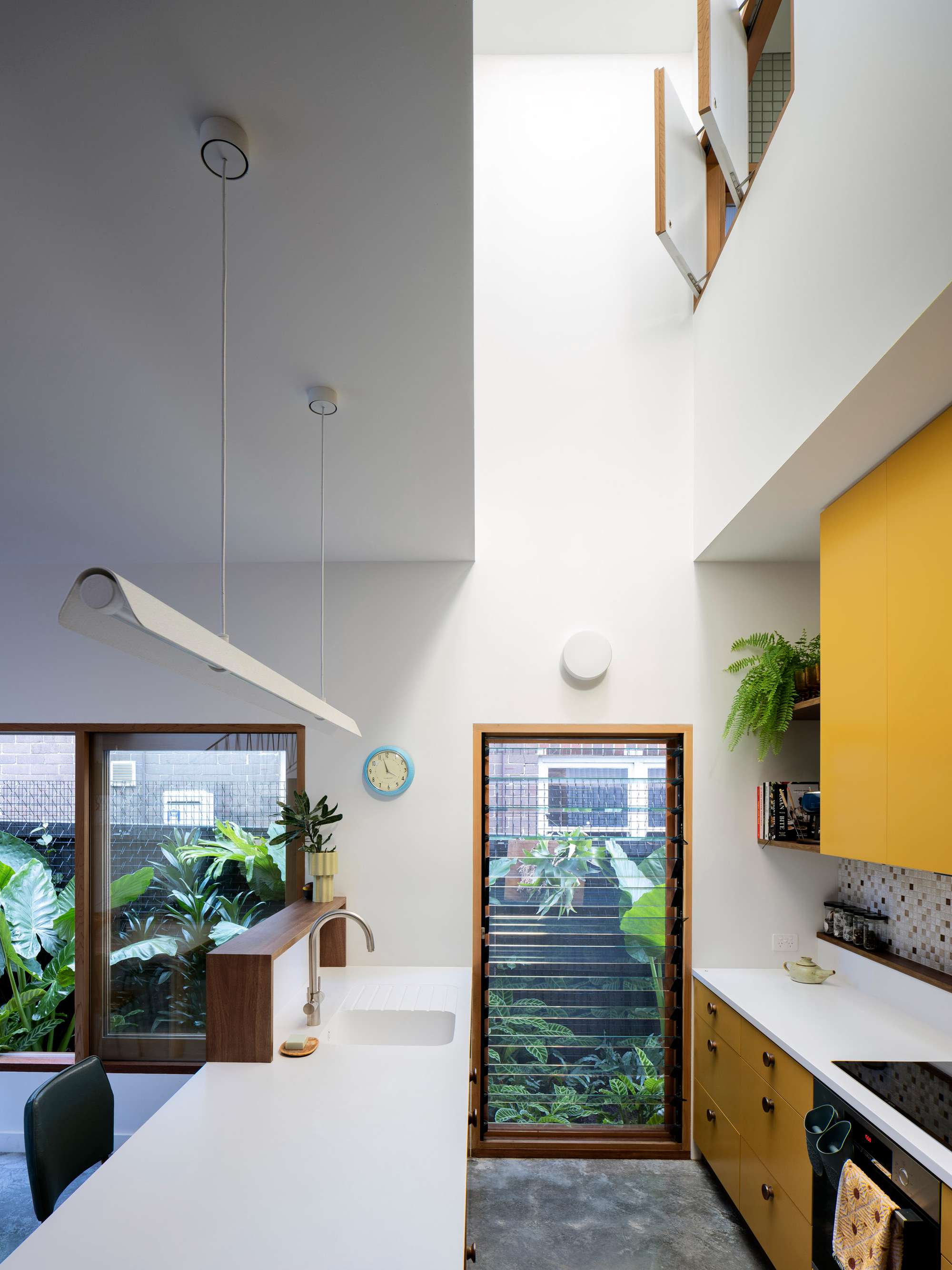 Fondue House by Castlepeake Architecture. Photography by Tom Ferguson. Kitchen with polished concrete floors, yellow cabinetry, white countertops, mosaic splashback and timber framed windows with louvres. 
